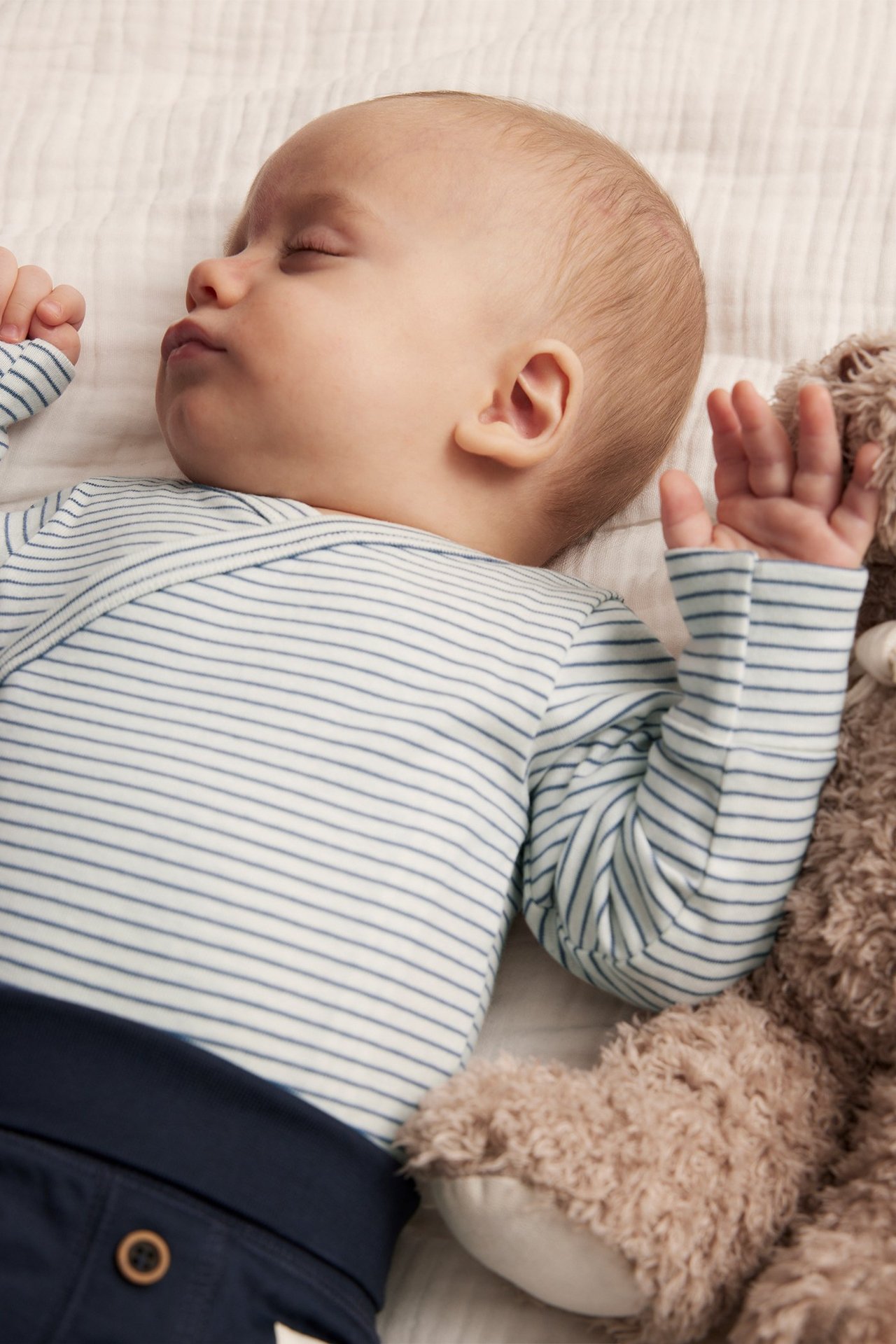 Lähikuva nukkuvasta vauvasta vaaleansinisessä raidallisessa pitkähihaisessa puuvillabodyassa ja tummansinisissä housuissa.