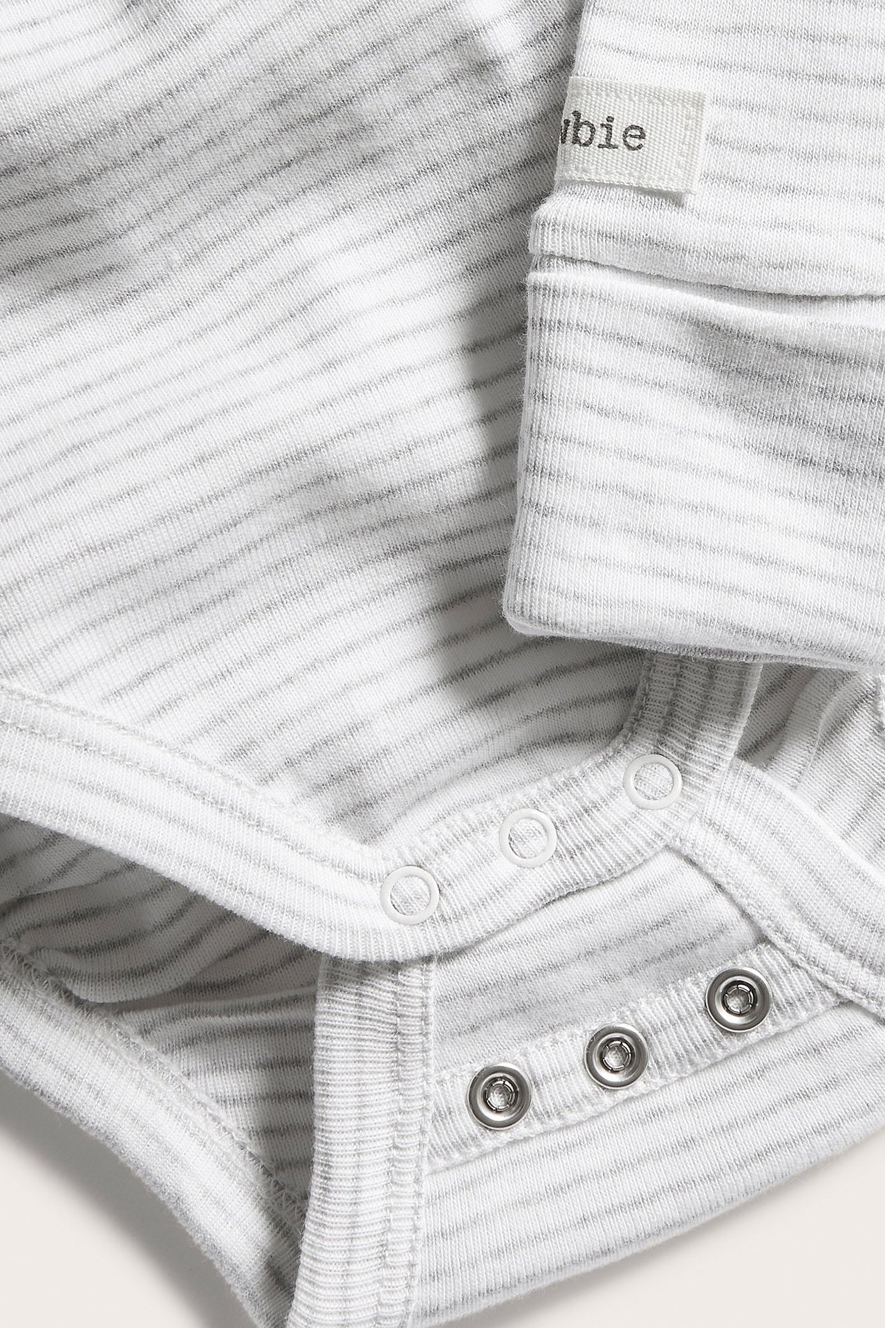 Närbild på babyrandig melerad grå bomullsbody med omlottknäppning och tryckknappar.