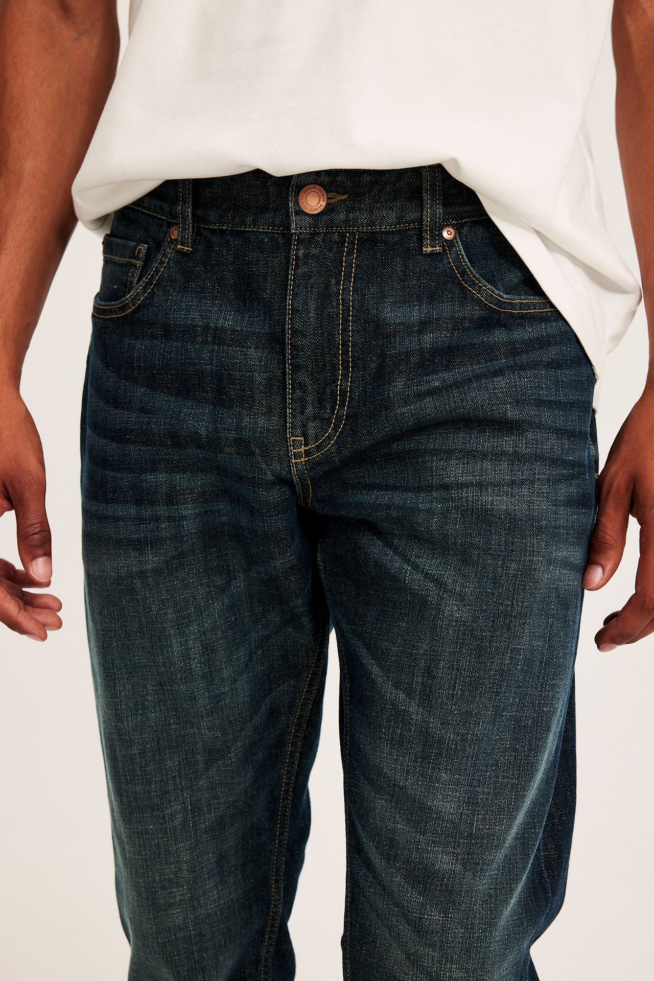 Framsida av man i blåa regular fit denimjeans med knapp och vit t-shirt.