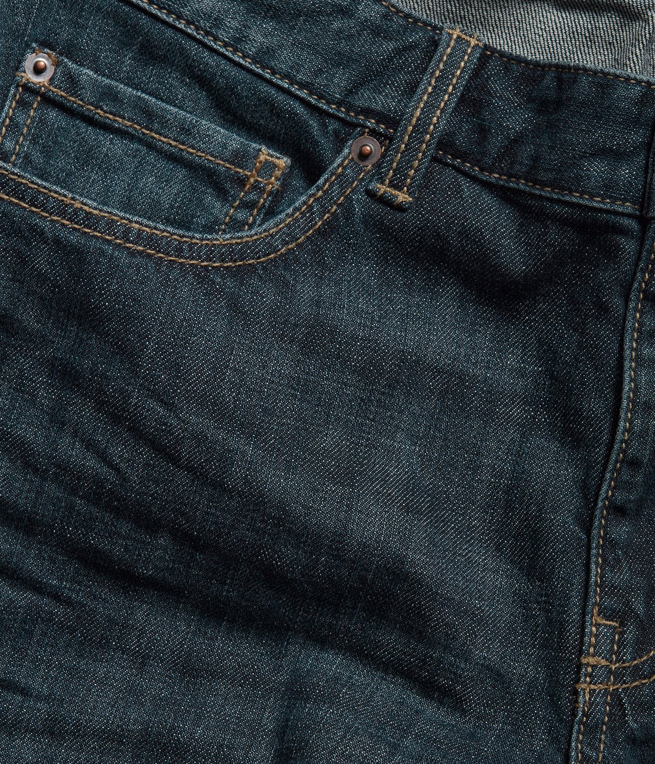 Zbliżenie na męskie jeansy regular fit z ciemnoniebieskiego denimu, z kontrastowymi szwami i nitami.