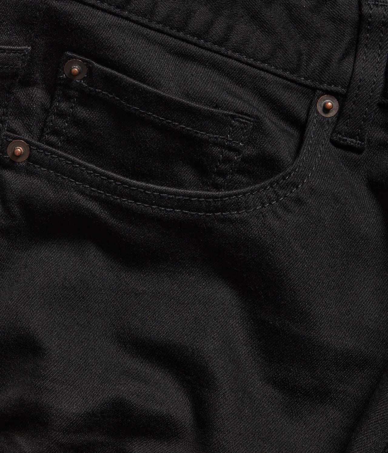 Zbliżenie czarnych jeansów regular fit, pokazujące przednią kieszeń z miedzianymi nitami.