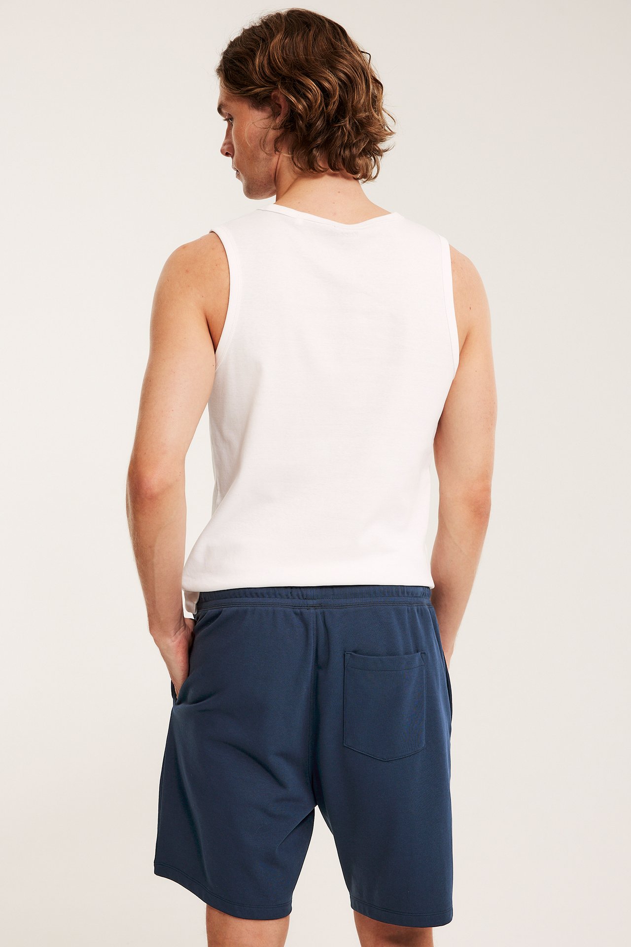 Ryggvy av en man i mörkblå mjukisshorts i sweatshirtmaterial med fickor och vitt linne.