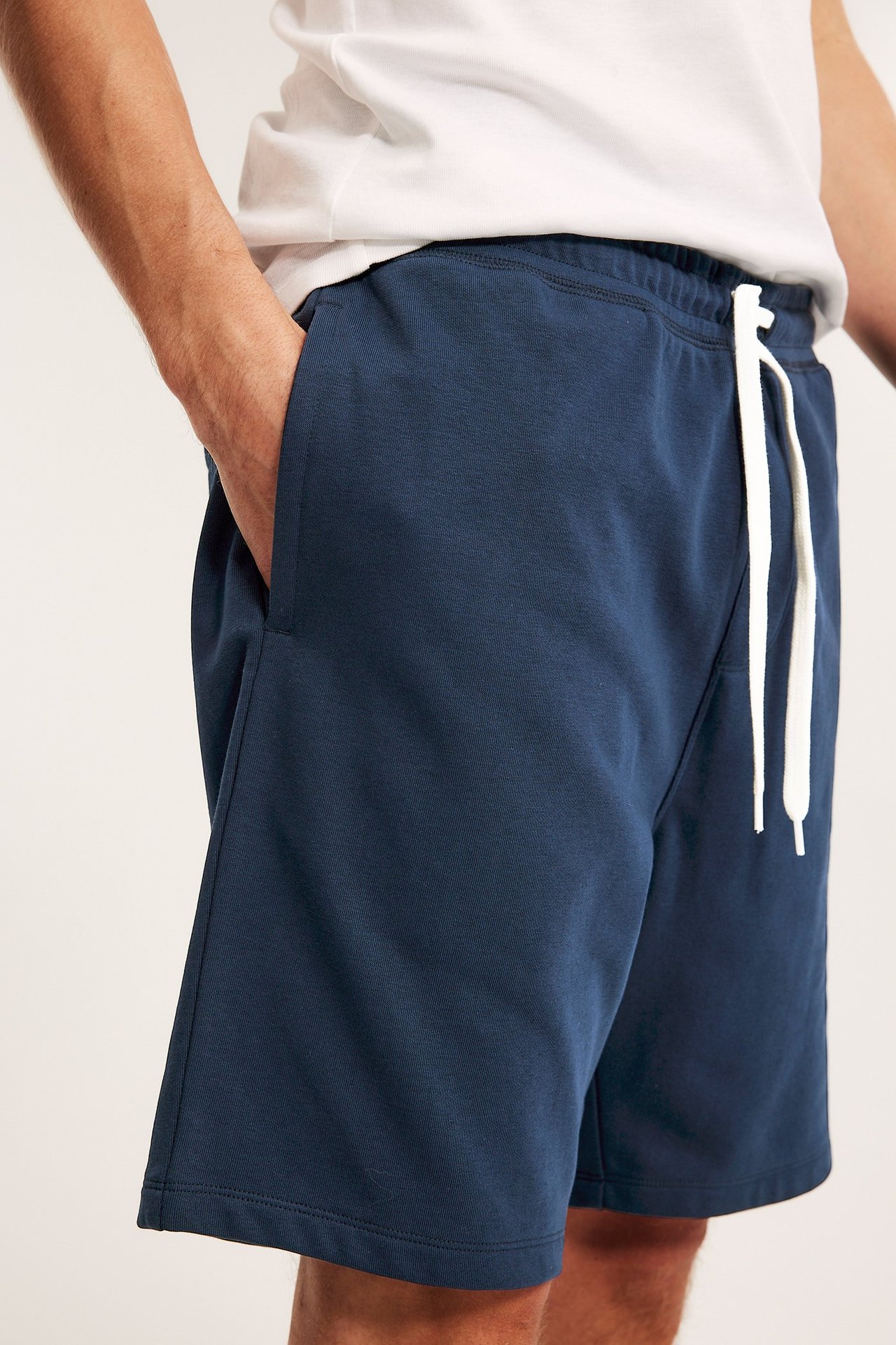 Man i mörkblå mjukisshorts med vit dragsko, sidfickor och en vit t-shirt.