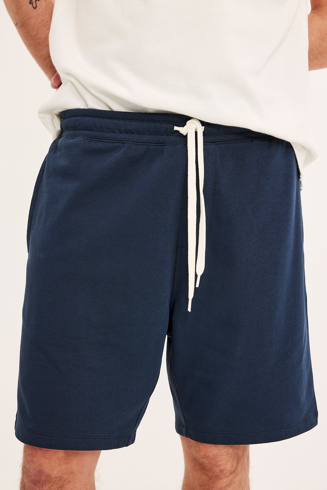 Edestäpäin: mies yllään tummansiniset college-shortsit valkoisella kiristysnyörillä ja valkoinen t-paita.