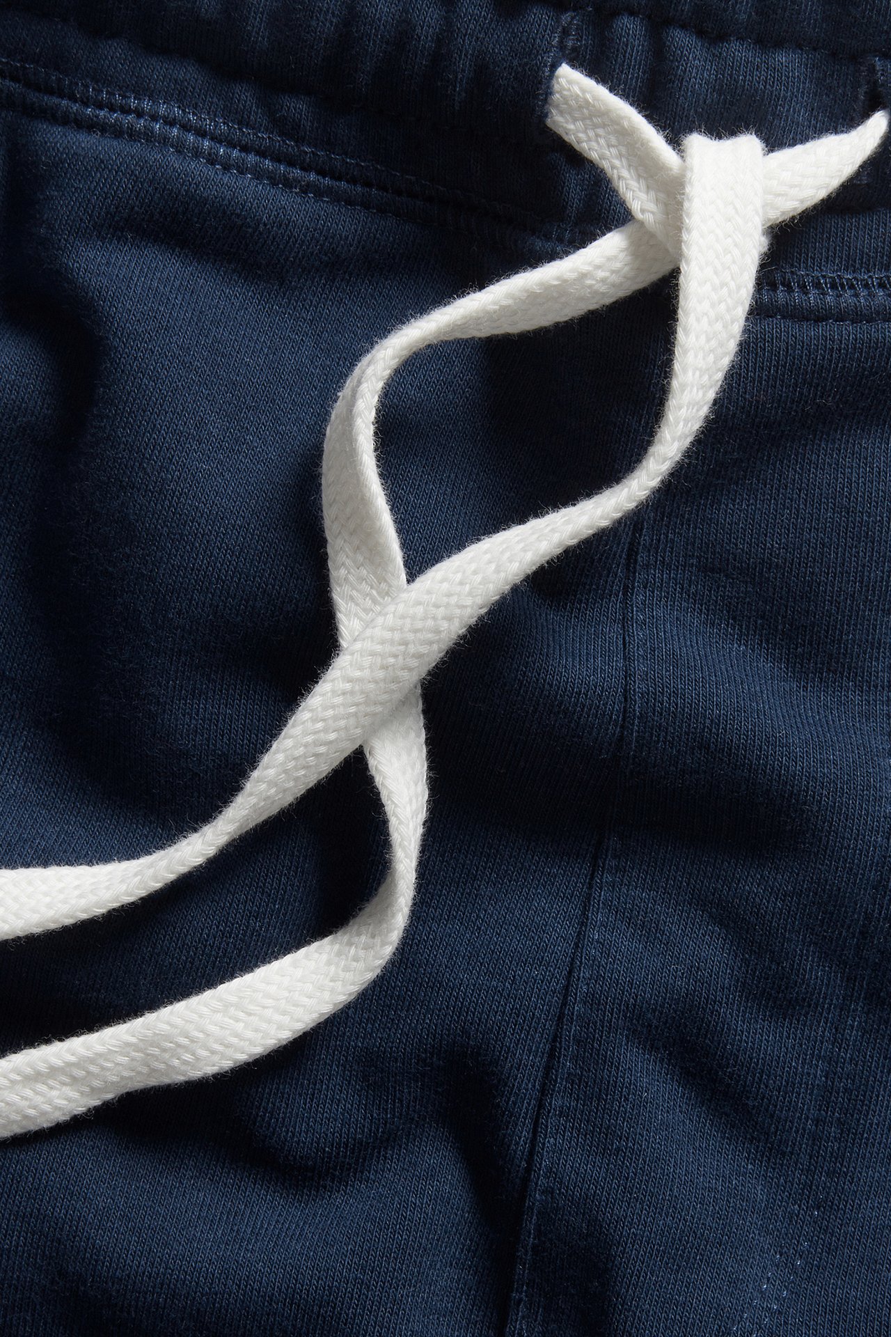 Zbliżenie ciemnoniebieskich szortów dresowych z białymi sznurkami zawiązanymi na elastycznej talii.