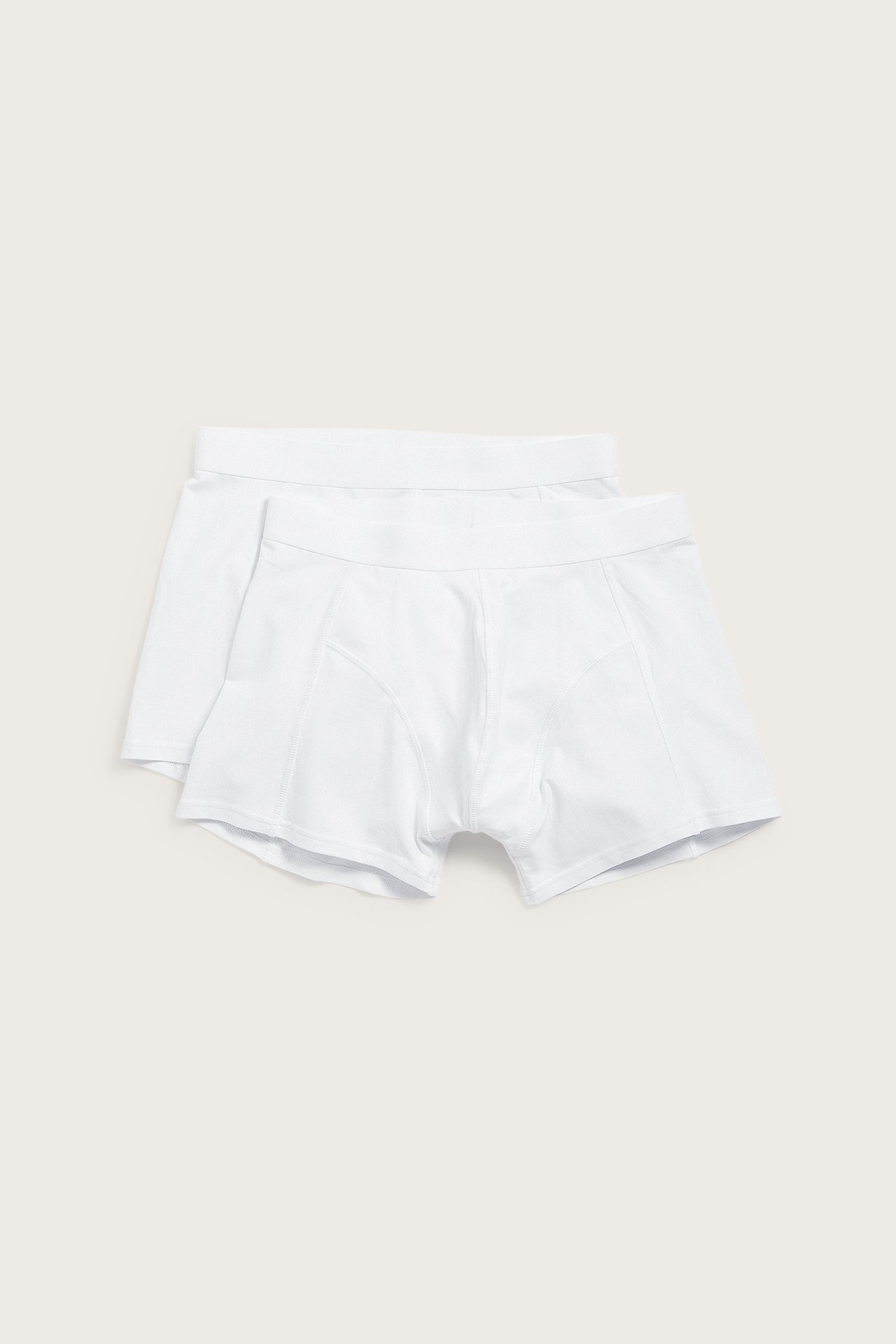 Framifrån, två vita enfärgade bomullsboxerkalsonger för män med normal benlängd, staplade.