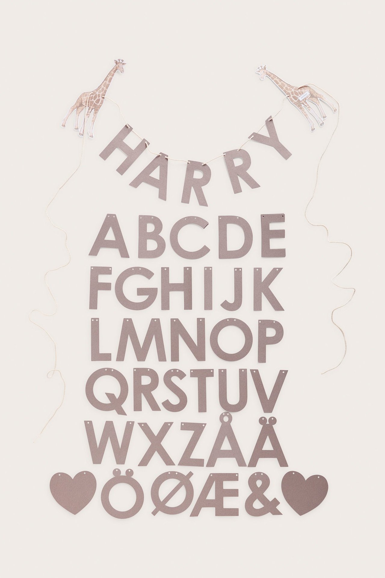 Ovenfra: brunt papirgirlandesett med bokstaver, to mønstrede sjiraffer og snor.