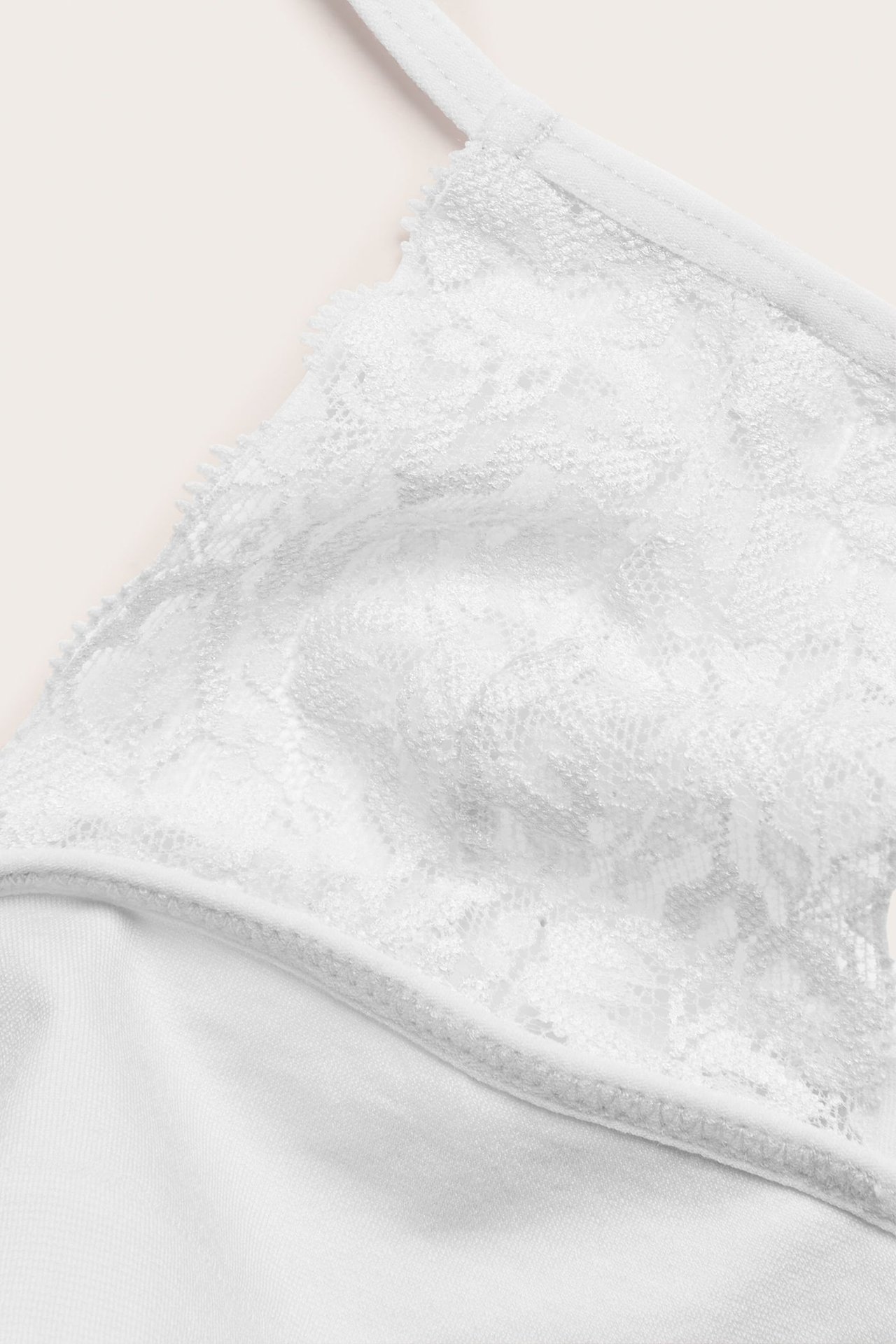 Nærbilde av en hvit blonde-trekants-bralette med tynn stropp og solid stoffbunn.