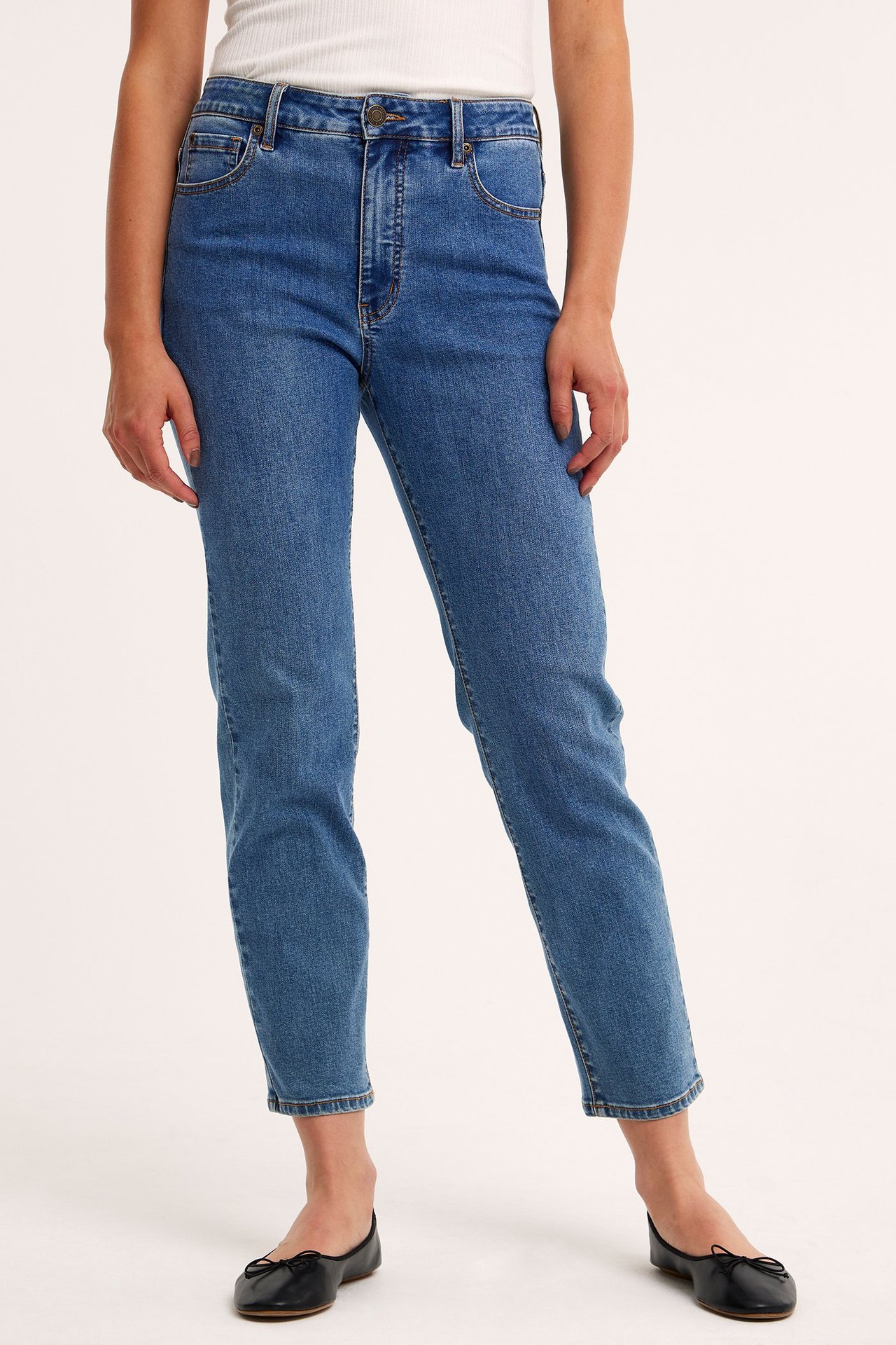 Framifrån: kvinna i blå denim raka jeans med hög midja, vit ribbad topp och svarta ballerinaskor.