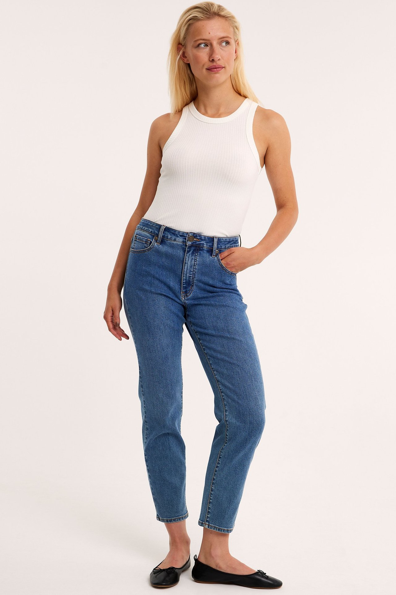 Framifrån: kvinna i blå raka jeans med hög midja, vit ribbad tanktopp och svarta ballerinaskor.
