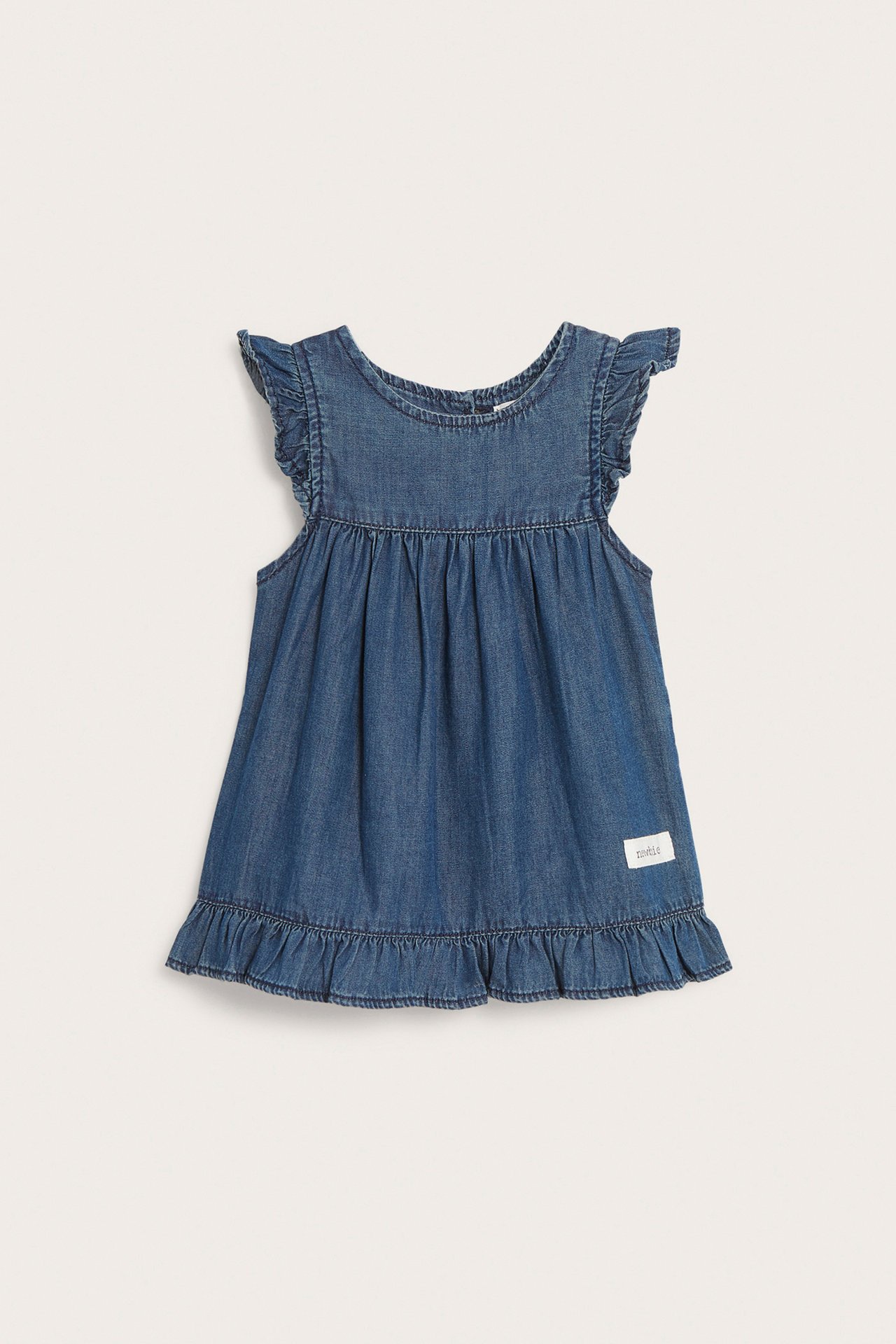 Frontbilde av en baby sin blå denimkjole med volanger på skuldre og en volangkant i bomull.