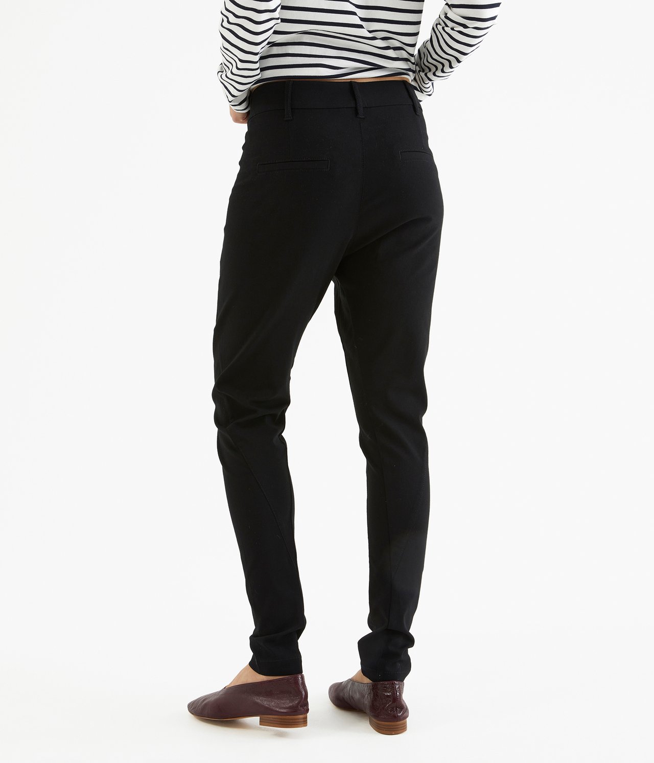 Widok z tyłu kobiety w czarnych spodniach boyfriend slim-fit, pasiastym topie i brązowych butach.