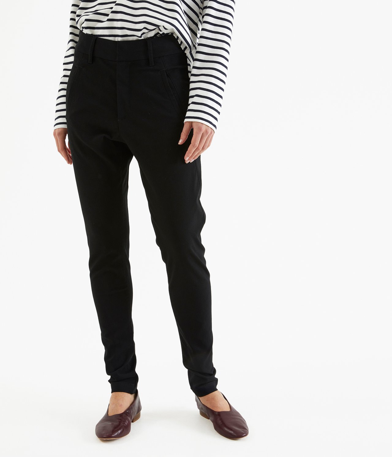 Widok z przodu kobiety w czarnych spodniach slim fit, bluzce w paski i bordowych płaskich butach.