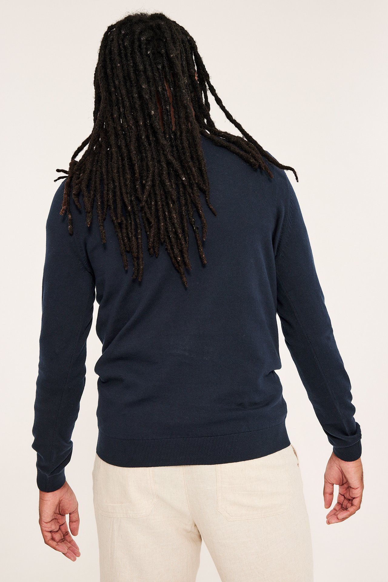 Bakifrån: man i mörkblå finstickad bomullströja med enfärgat mönster och ljusbeige byxor.