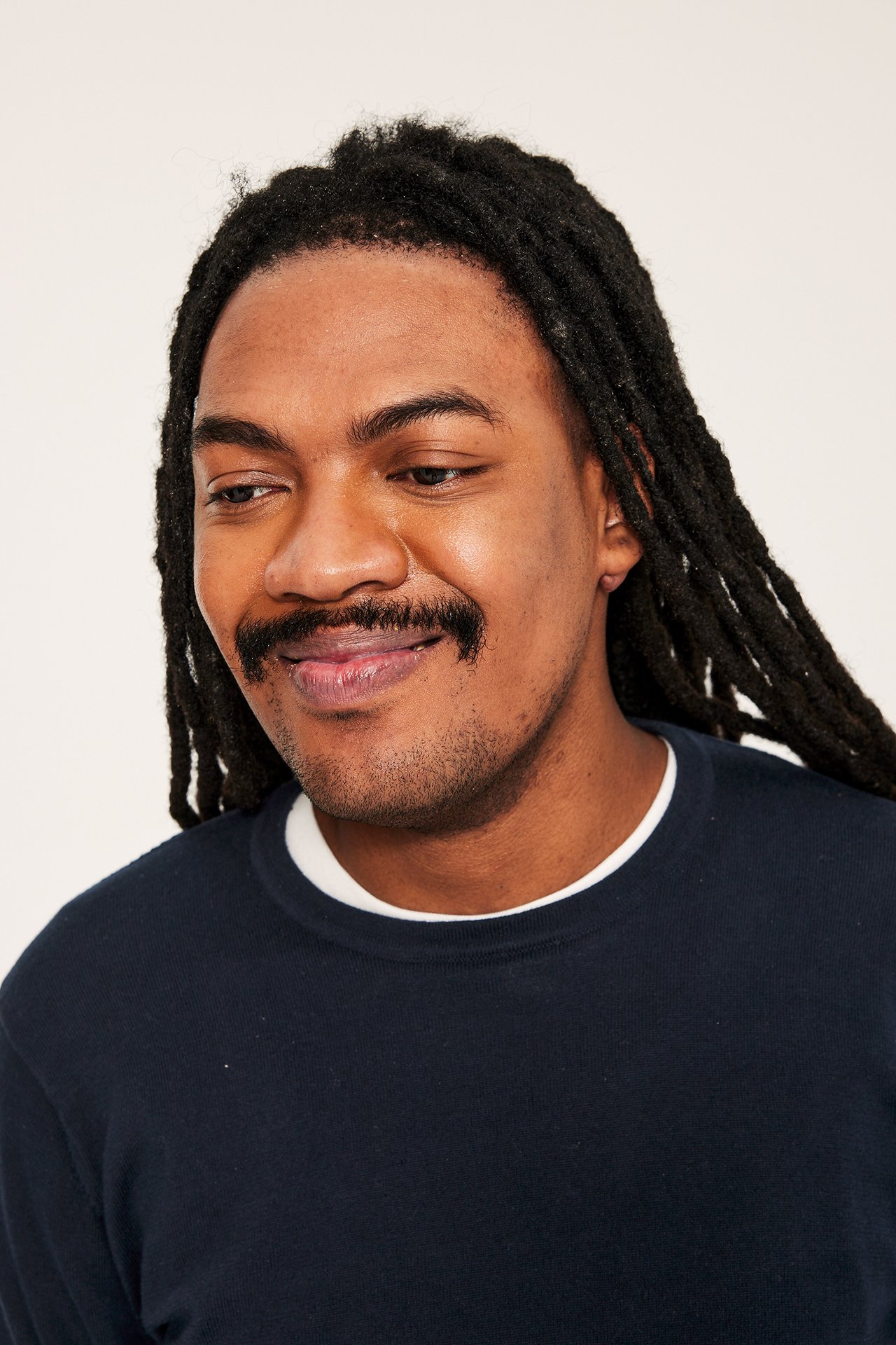 Närbild på en man i en mörkblå finstickad bomullströja över en vit t-shirt.