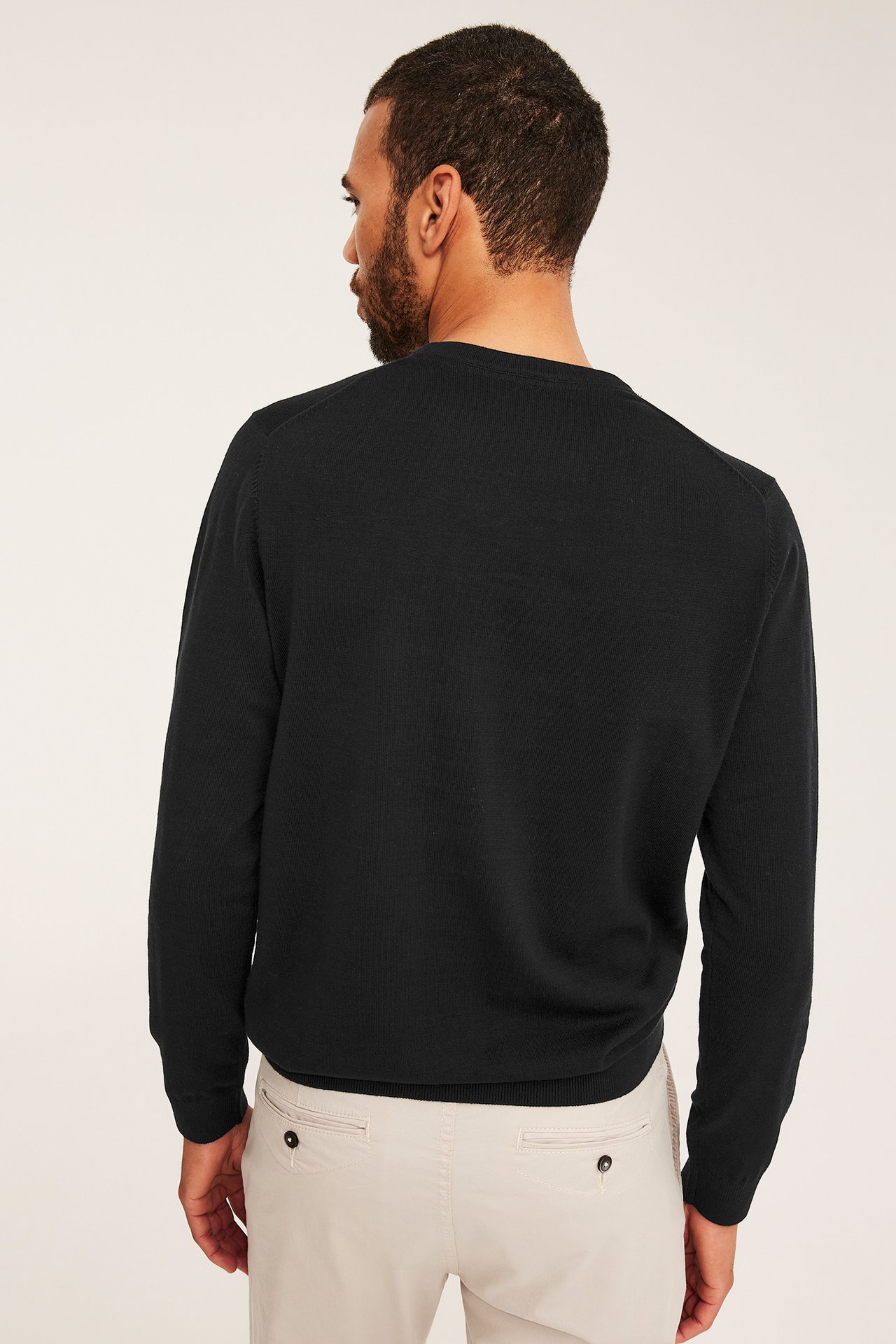 Widok z tyłu mężczyzny w czarnym, drobno dzianym bawełnianym swetrze i beżowych spodniach.
