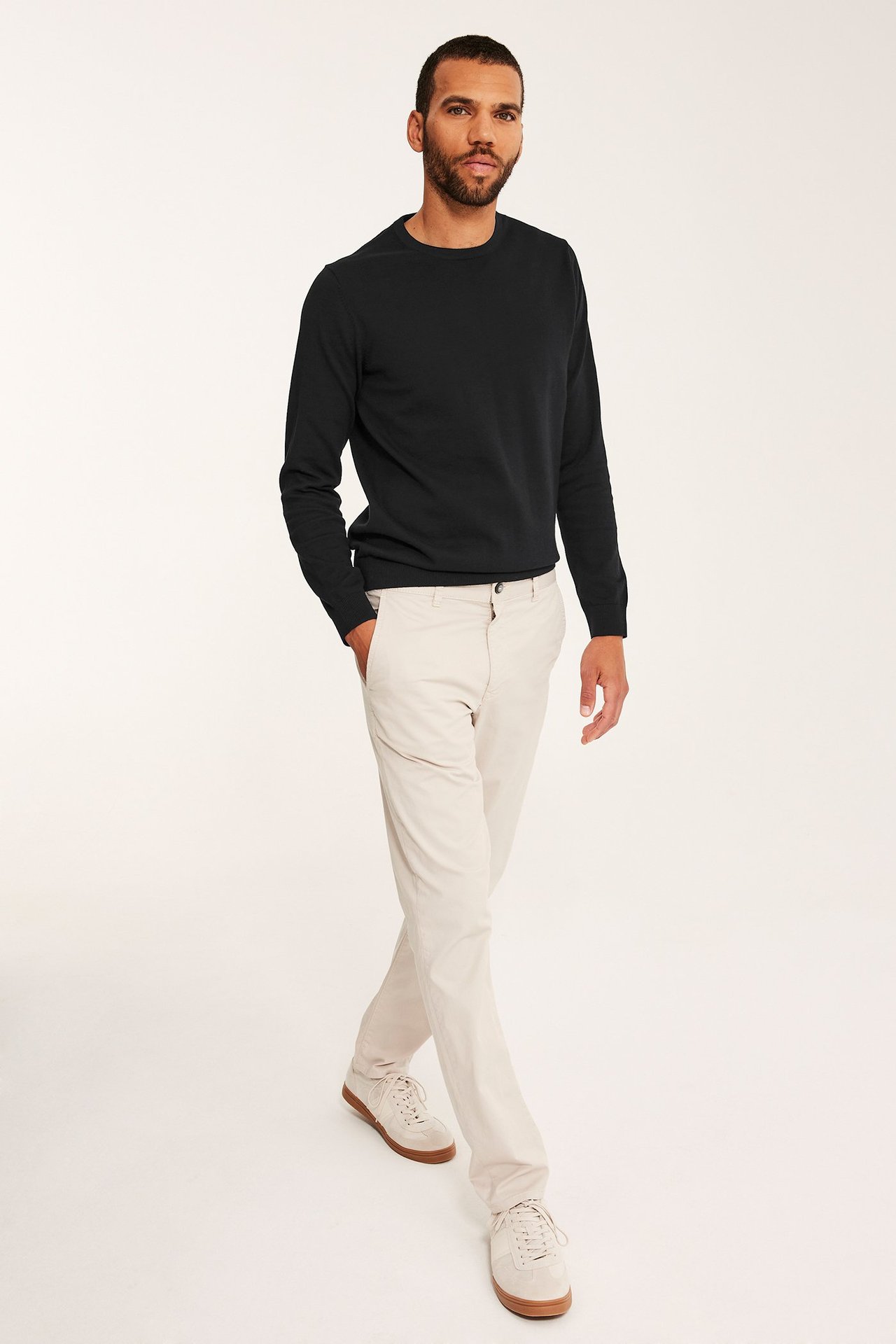 Widok z przodu: mężczyzna w czarnym, cienkim swetrze bawełnianym, jasnobeżowych chinosach i sneakersach.