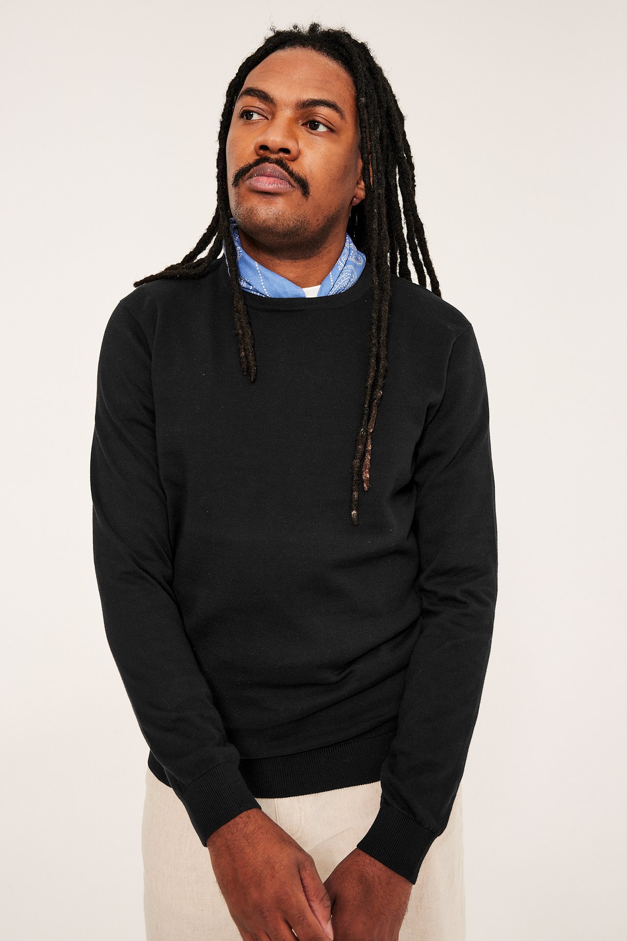 Widok z przodu mężczyzny w czarnym swetrze bawełnianym, niebieskiej bandanie i beżowych spodniach.