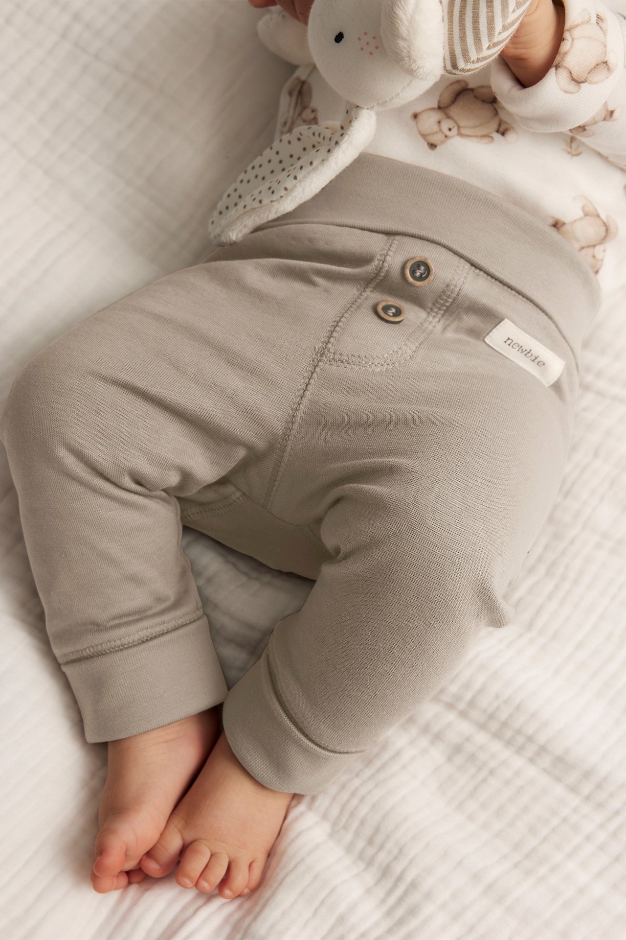 Närbild på baby i beiga bomullsleggings med dekorativa knappar, nedvikt midja och uppvikta muddar.