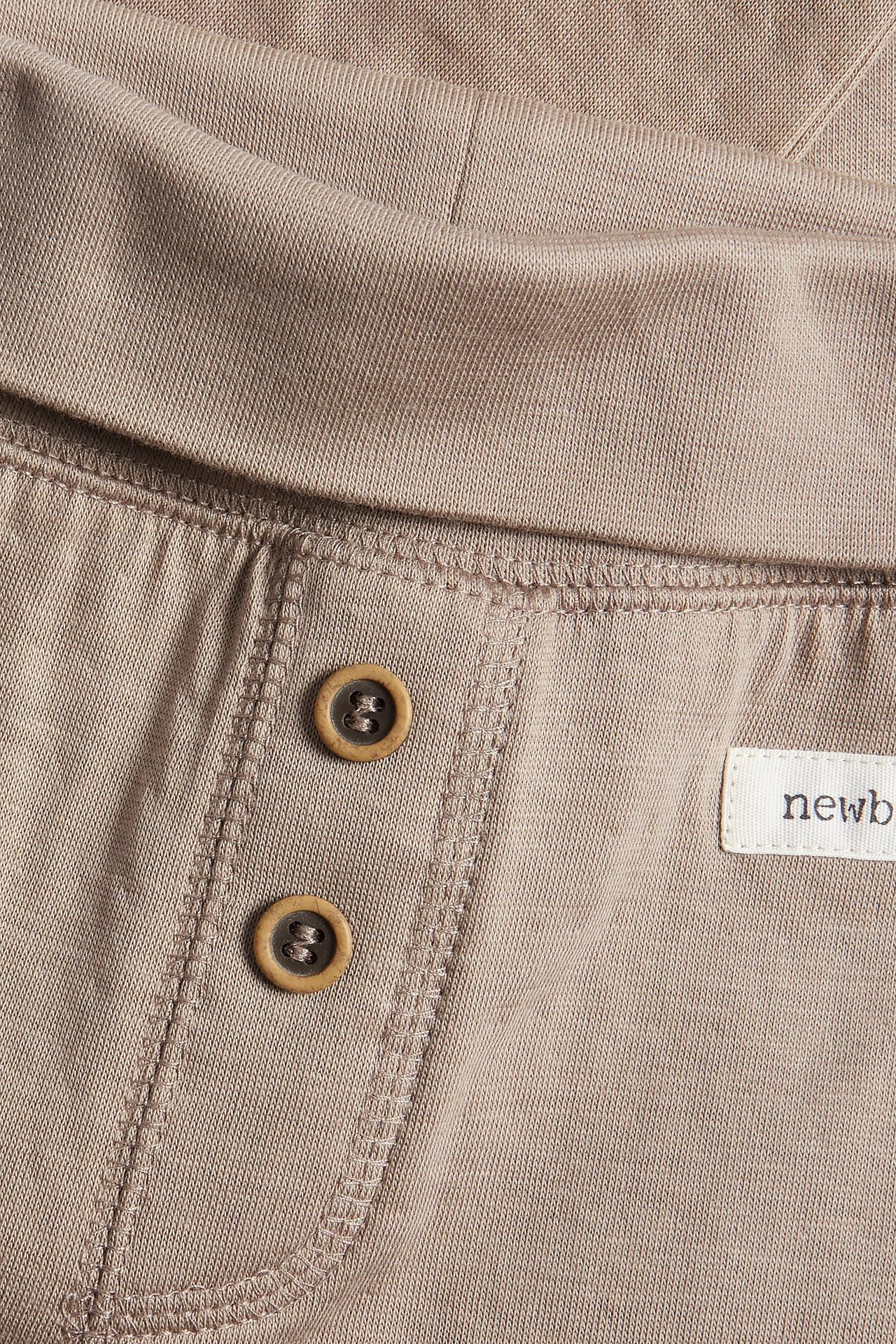 Zbliżenie beżowych bawełnianych legginsów niemowlęcych z wywijanym pasem i dwoma ozdobnymi guzikami.