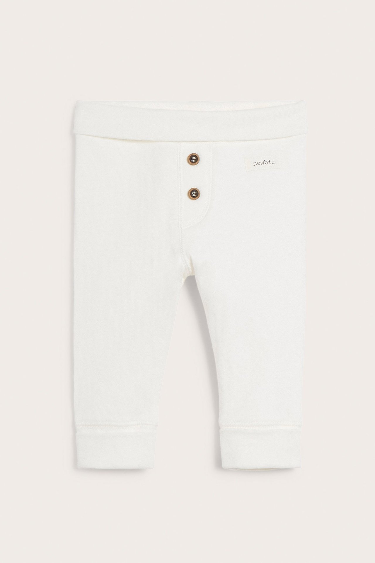 Framifrån av offwhite baby-leggings i bomull med nedvikt midja, dekorativa knappar och uppvikbara muddar.