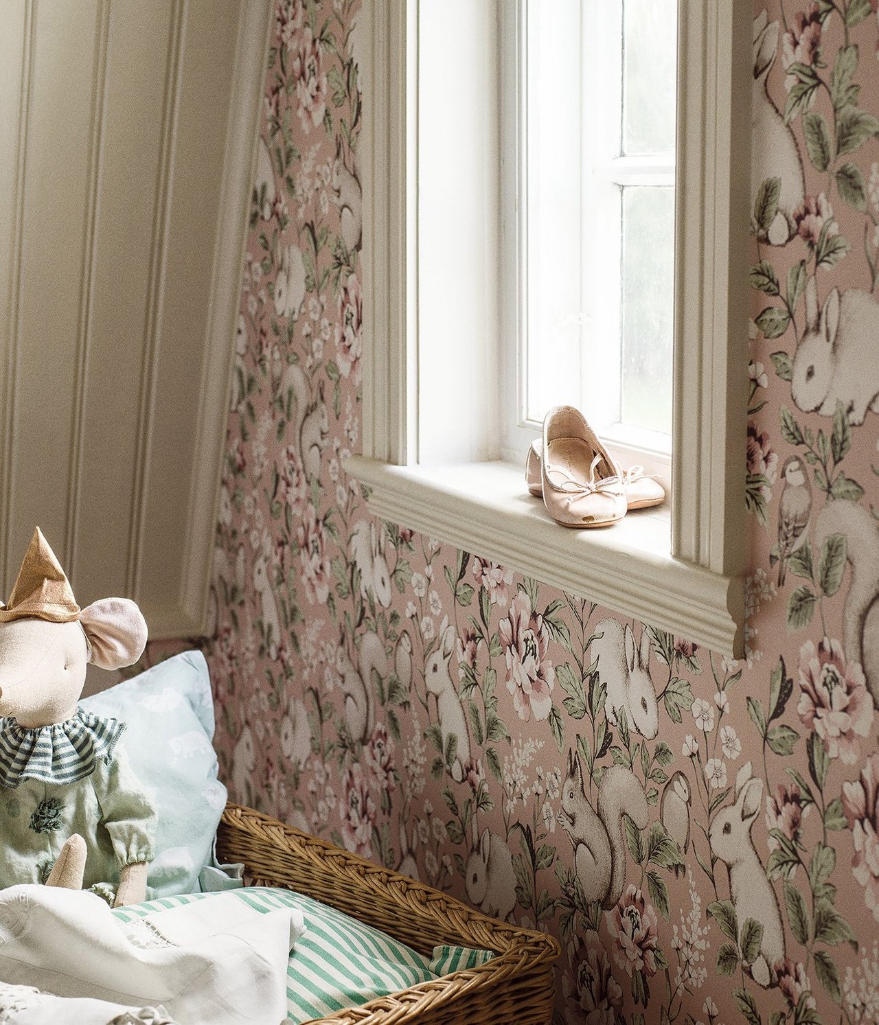 Różowa tapeta flizelinowa z królikami, wiewiórkami i kwiatami. Różowe balerinki na parapecie, mysz-zabawka w koszu.