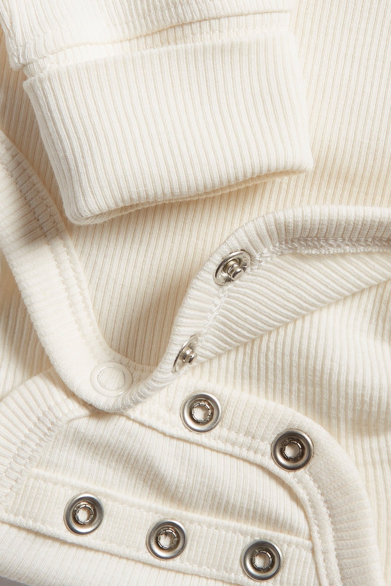 Zbliżenie na kremowe, prążkowane body niemowlęce z zatrzaskami i prążkowanymi mankietami.