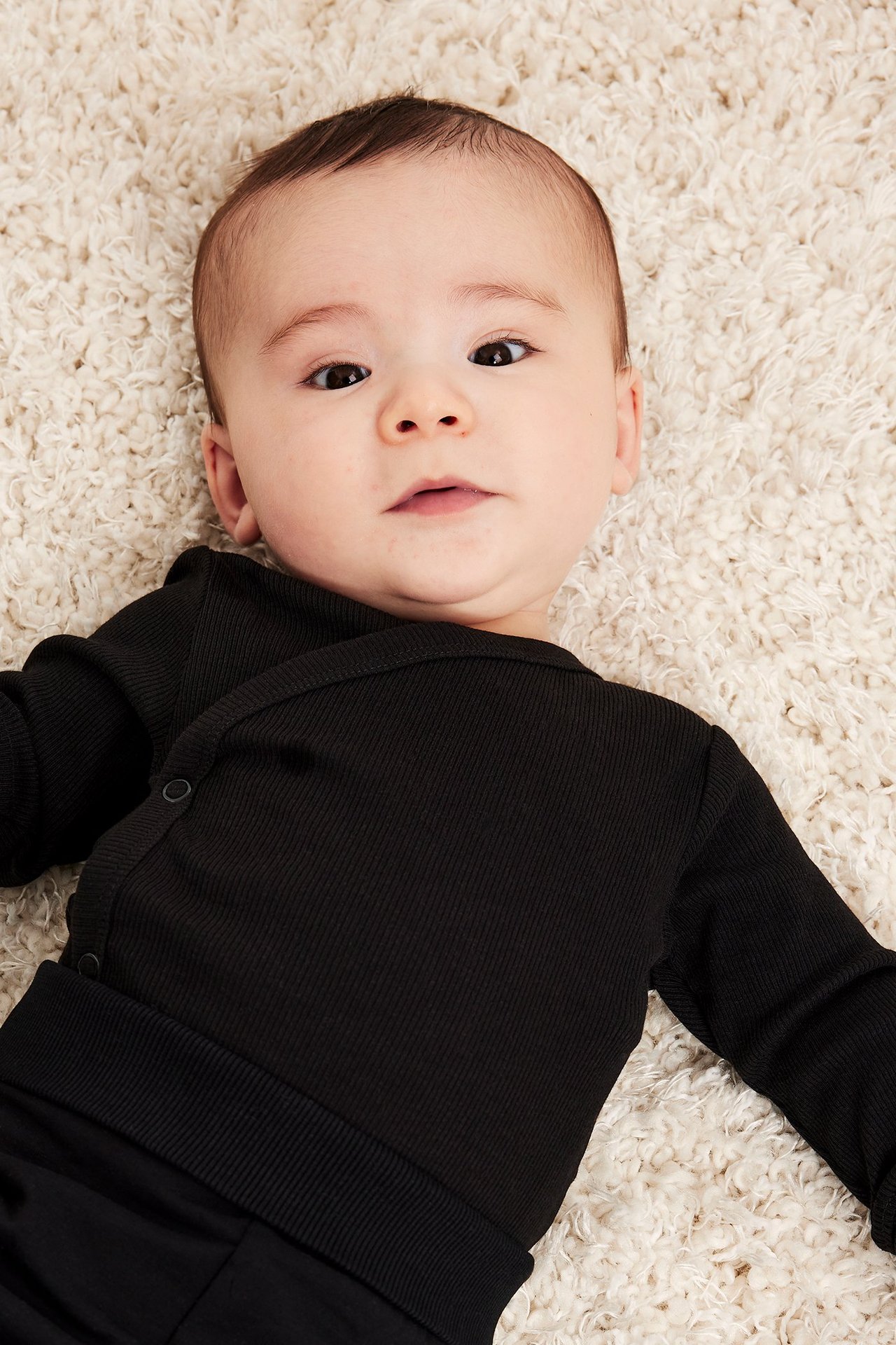 Ylhäältä kuvattu vauva mustassa ribatussa kietaisubodyssa, jossa sivunapit.