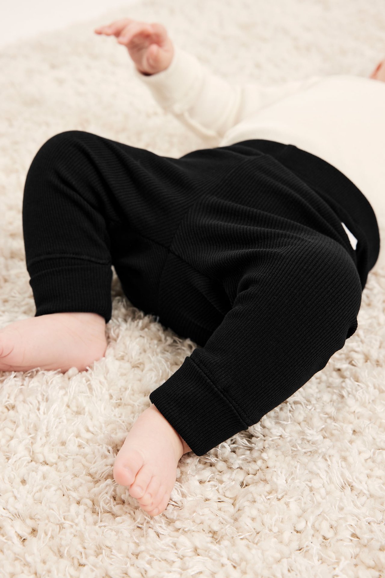 Ylhäältä, vauva mustissa ribatuissa leggingseissä reiluin resorein ja kermanvärisessä pitkähihaisessa paidassa.