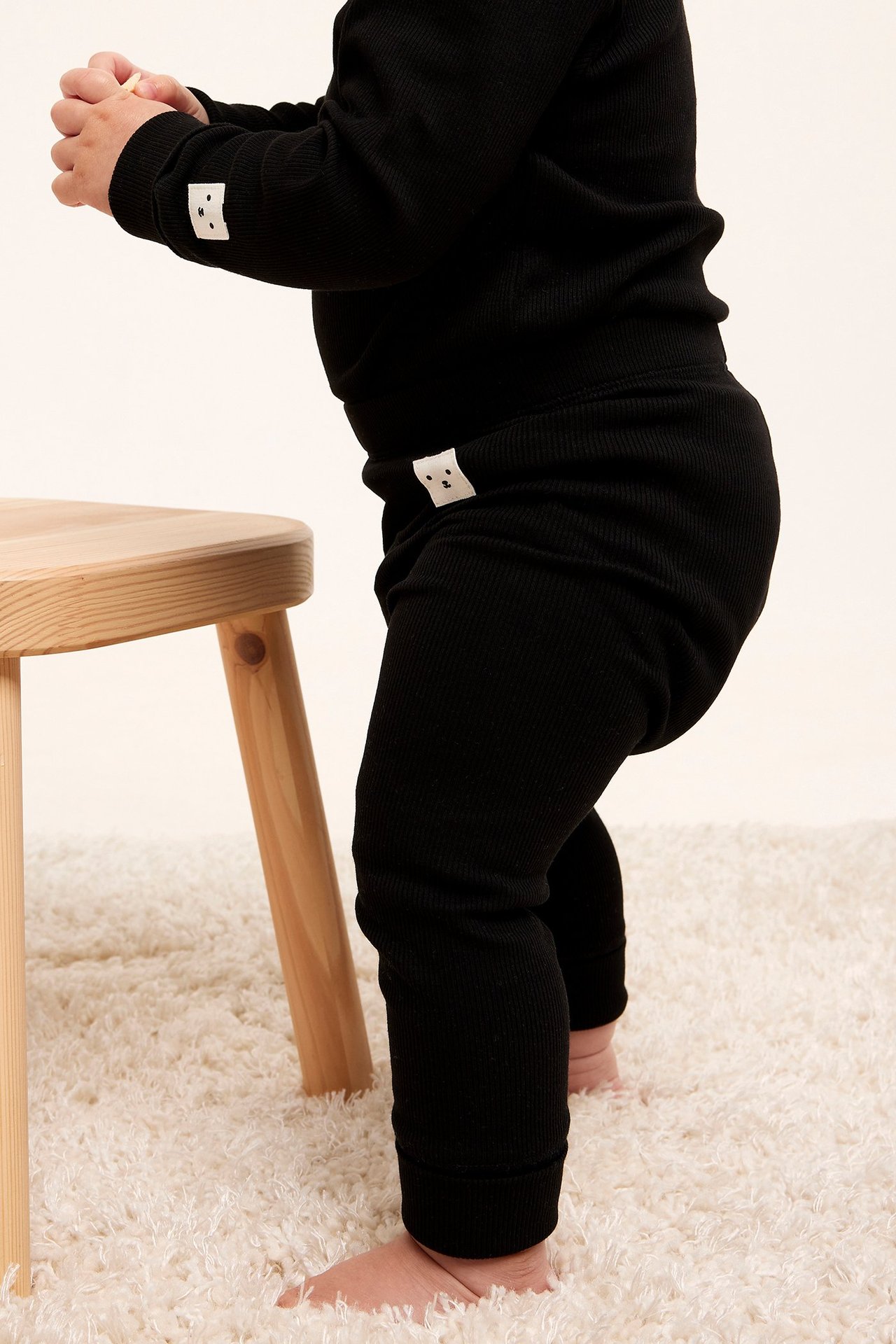 Sidovy av en baby i svarta ribbade leggings med generösa muddar och matchande långärmad topp.