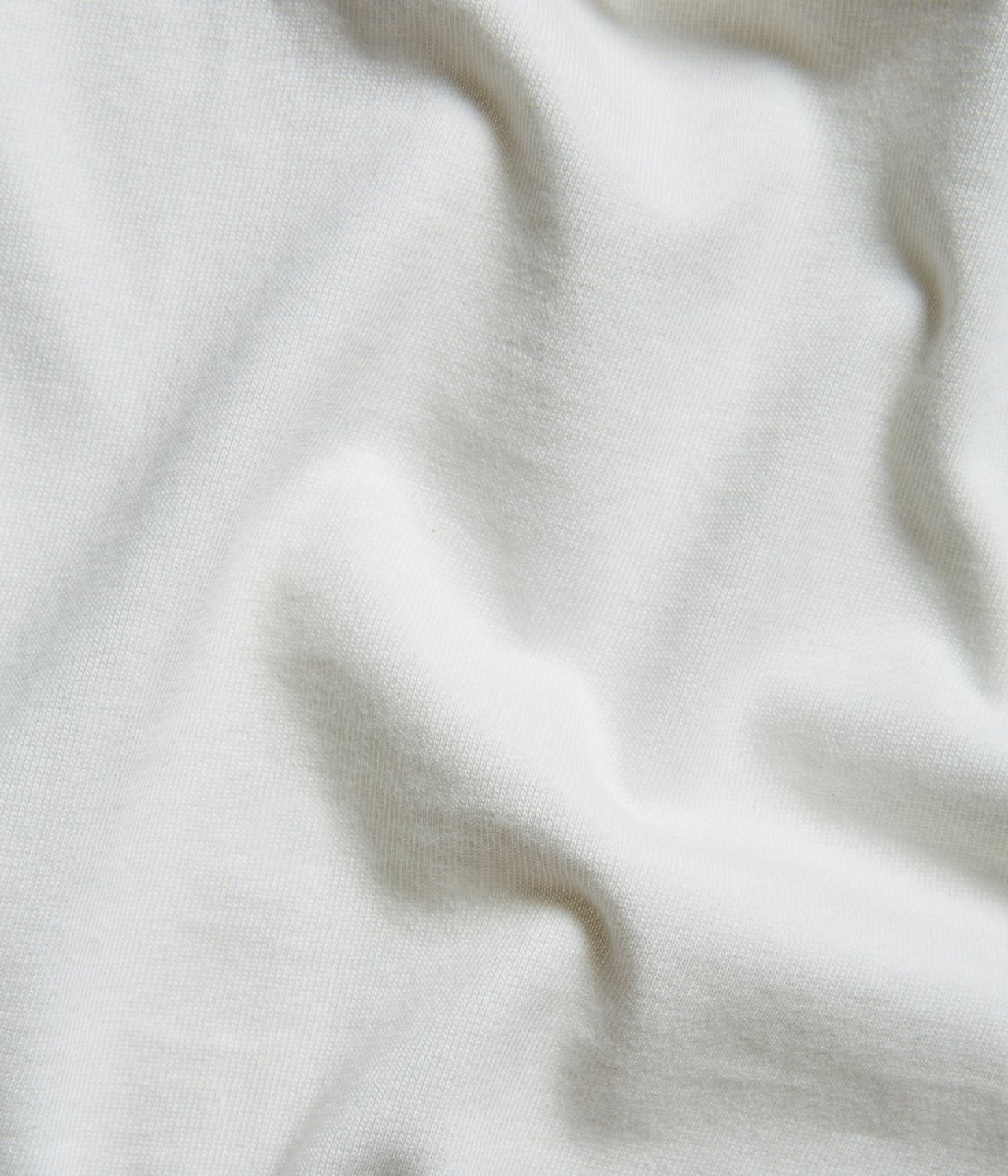 Zbliżenie na jednolity, kremowy materiał bawełnianej koszulki z widoczną teksturą i zagnieceniami.