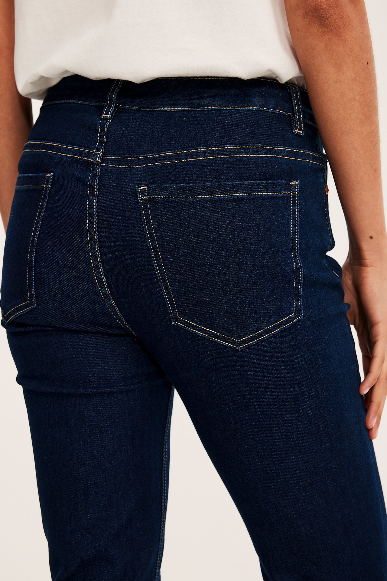 Widok z tyłu kobiety w ciemnych jeansach straight-fit z kontrastowymi szwami i białym t-shircie.