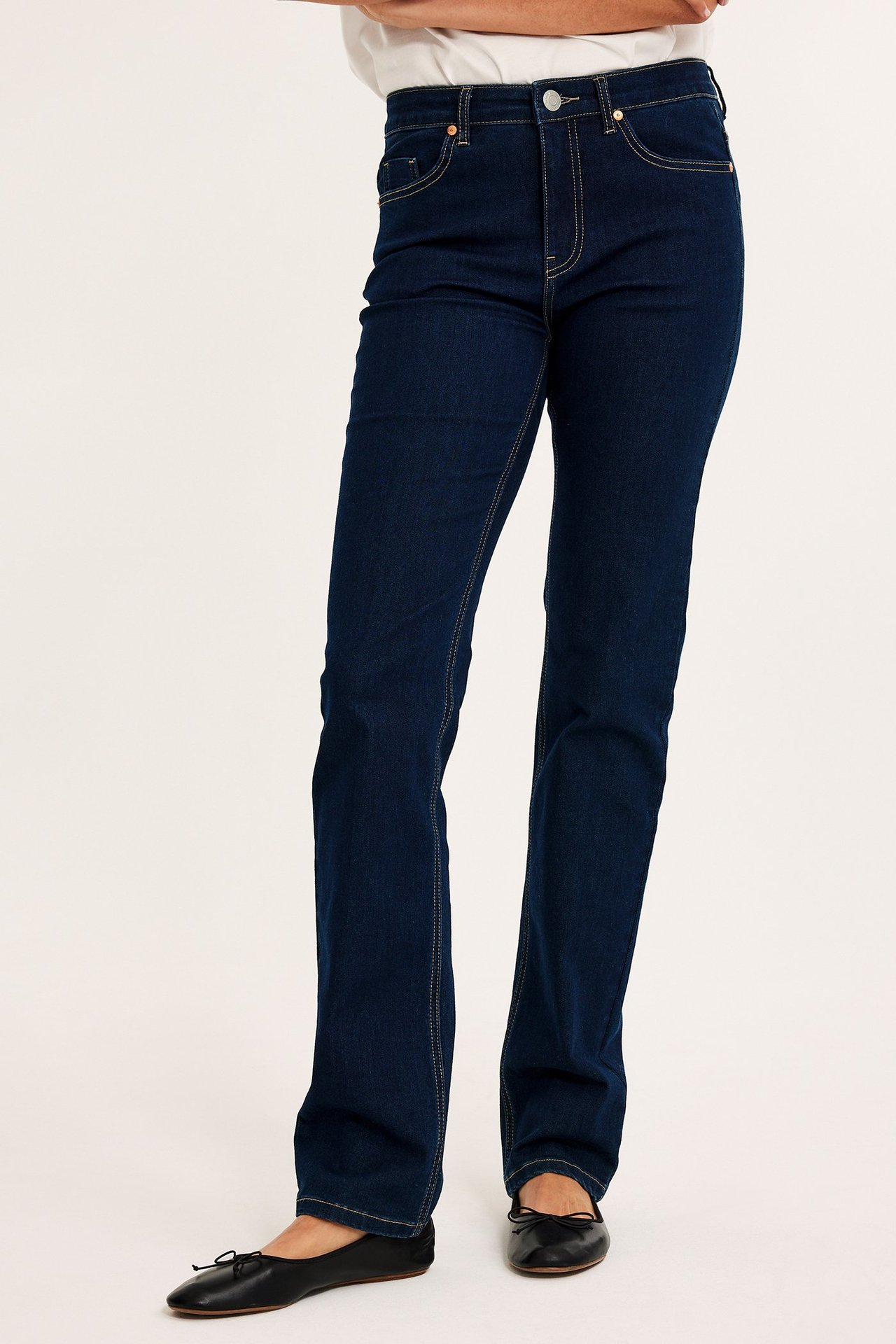 Framifrån, kvinna i mörkblå raka jeans, vit t-shirt och svarta ballerinaskor.