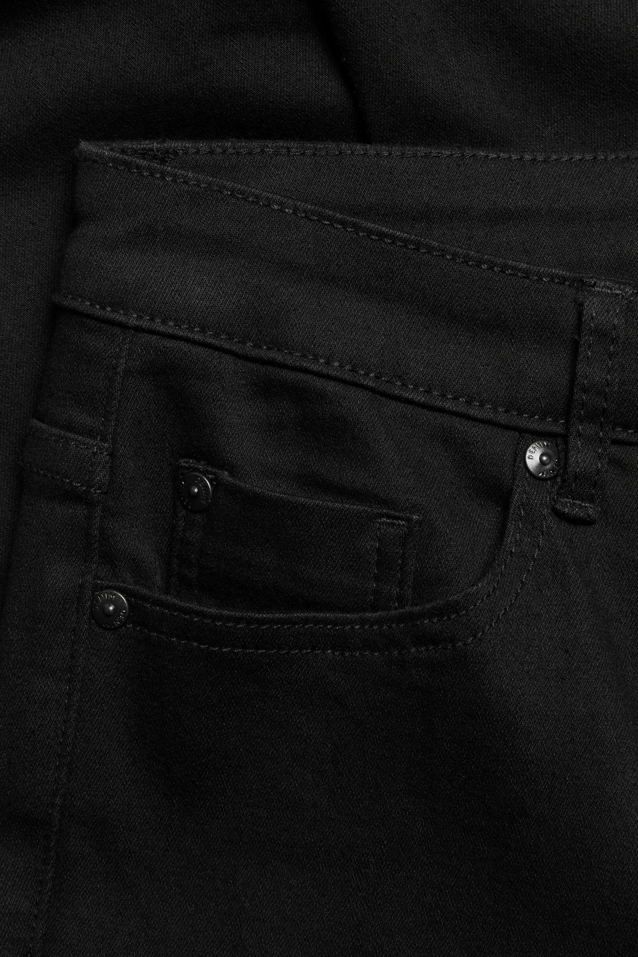 Zbliżenie na czarne proste jeansy denimowe, pokazujące przednią kieszeń z nitami i widocznymi szwami.