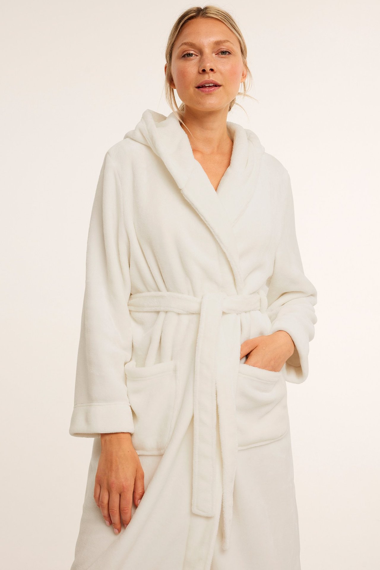Edestä näkymä naisesta valkoisessa hupullisessa fleecemorgonrockissa, jossa on vyö ja taskut.