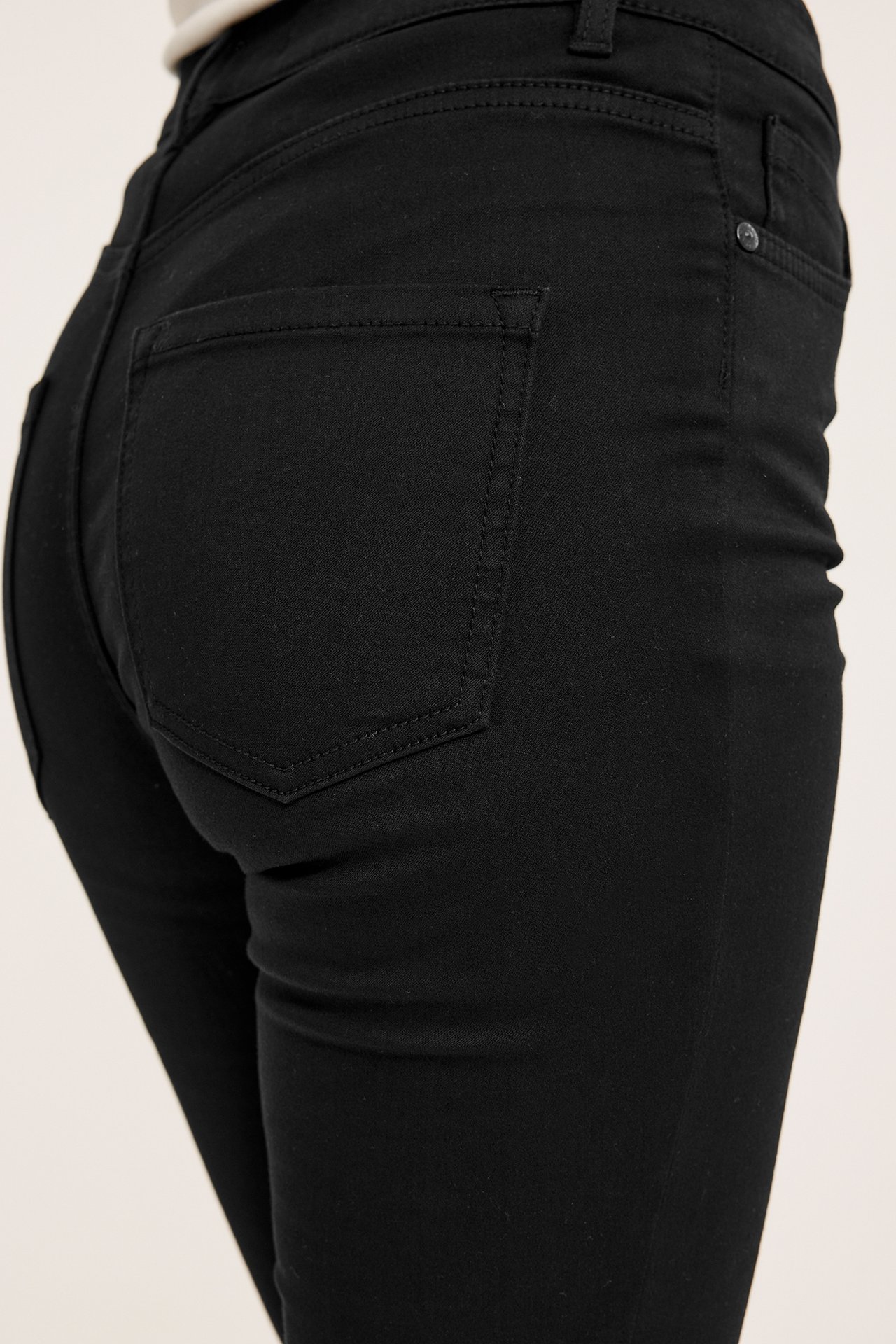 Nærbilde bakfra av en kvinne i svarte supersmale jeans med synlige baklommer.