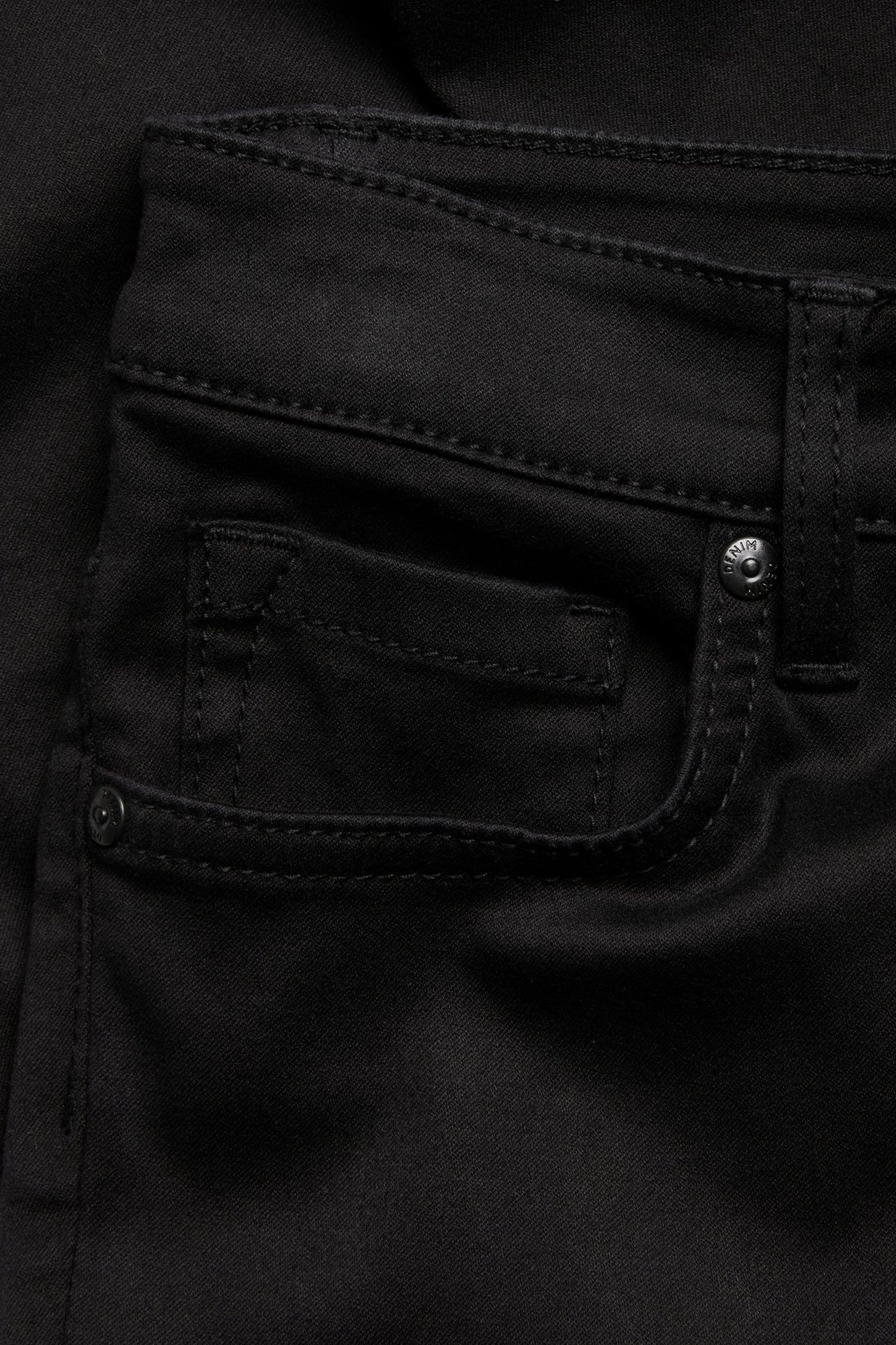 Zbliżenie na czarne jeansy super slim, pokazujące przednią kieszeń ze szwami i metalowym nitem.