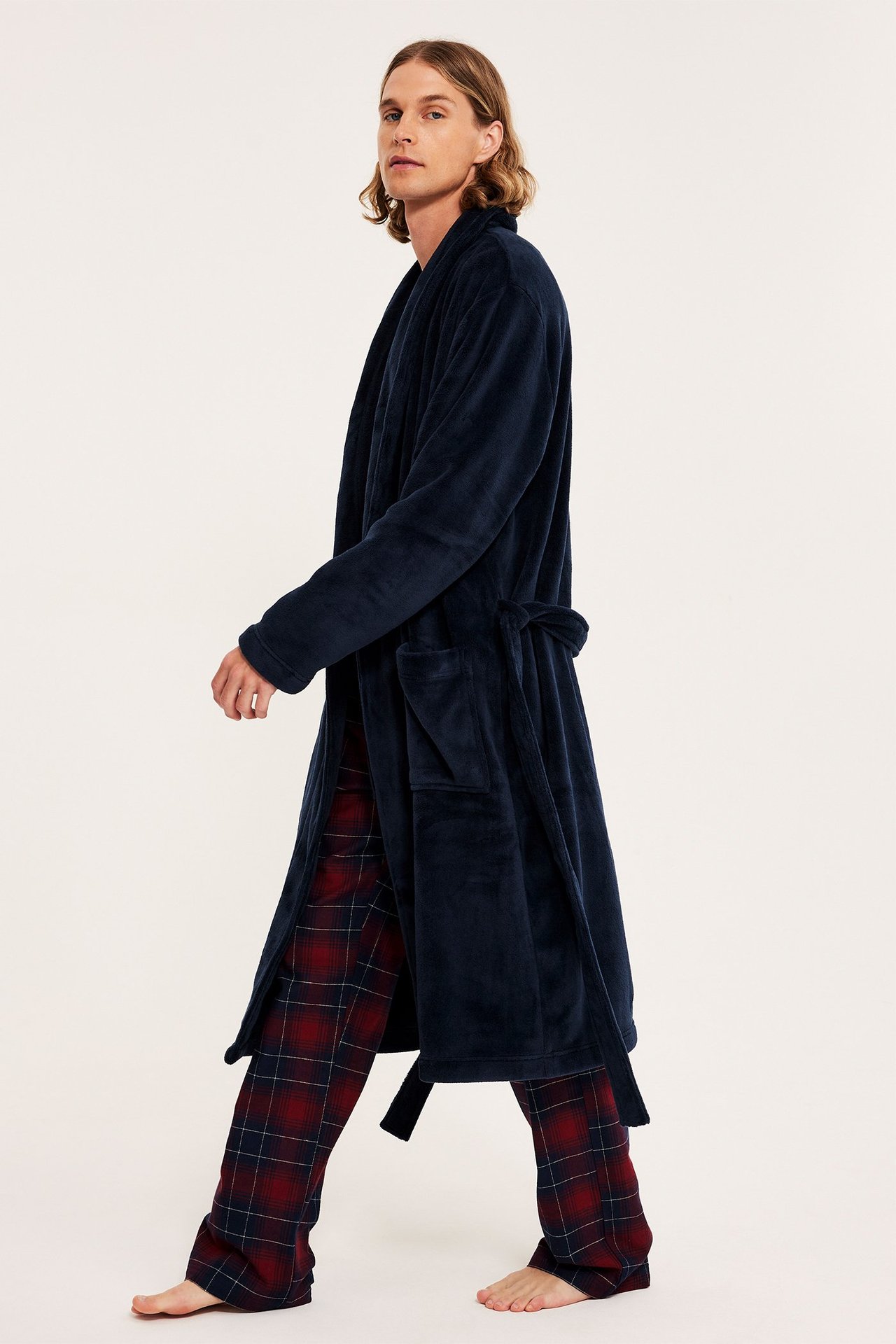 Widok z boku mężczyzny w granatowym szlafroku polarowym z kieszeniami, na czerwonych spodniach w kratę.