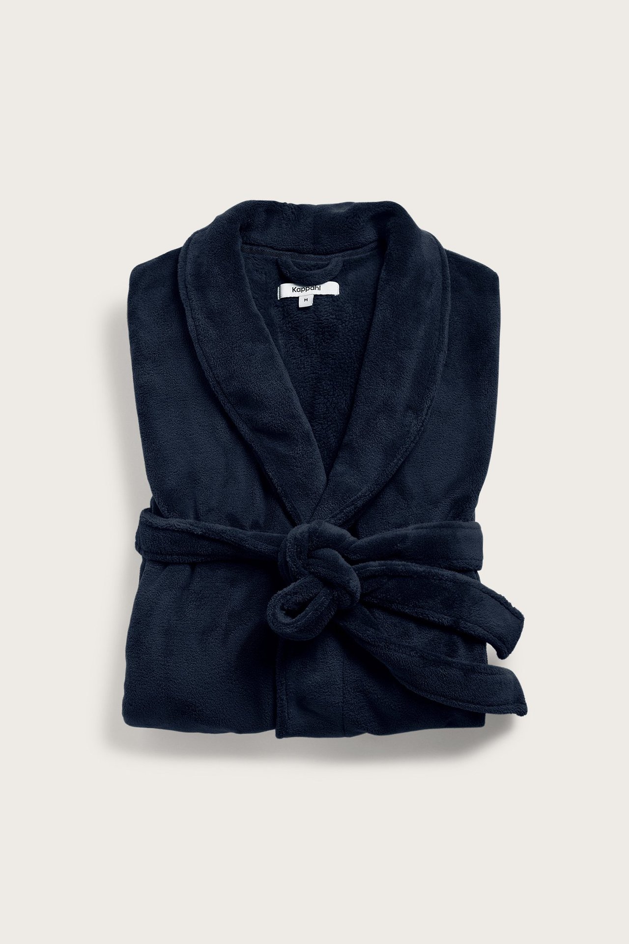 Widok z przodu złożonego, granatowego, jednolitego szlafroka polarowego z kołnierzem szalowym i wiązanym paskiem.