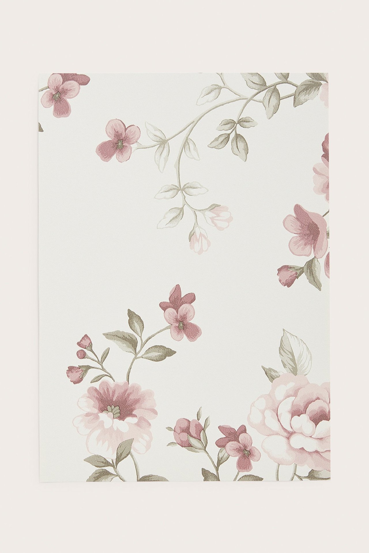 Nærbilde av en offwhite non-woven tapetprøve med et rosa blomstermønster.