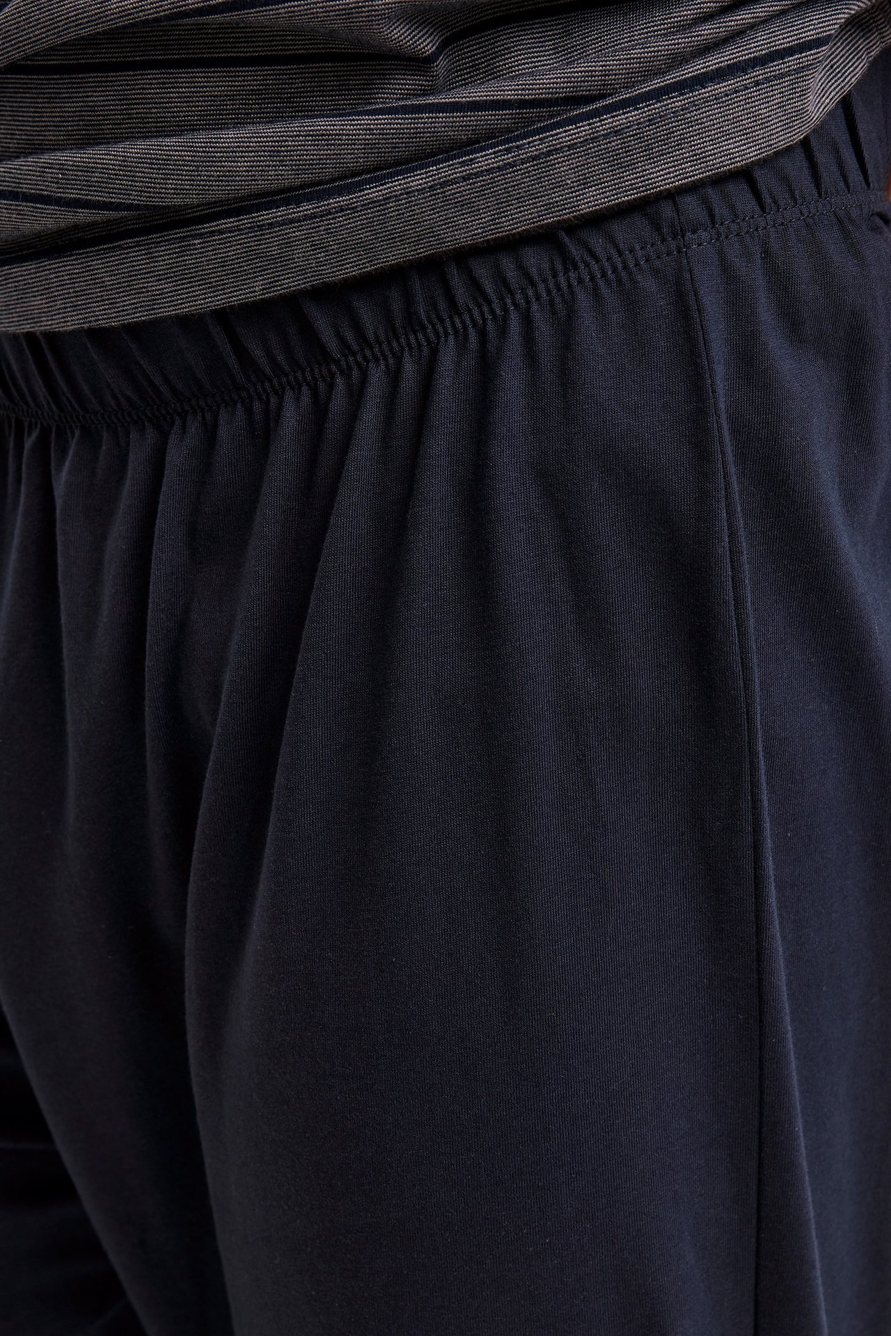 Lähikuva tummansinisistä puuvillatrikoopyjamahousuista, joissa on joustava vyötärö, raidallisen paidan kanssa.