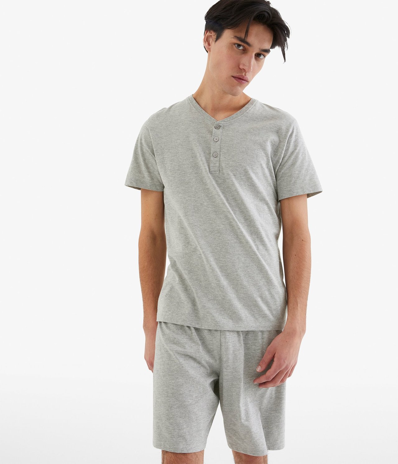 Edestä näkymä miehestä yllään vaaleanharmaa meleerattu jersey-pyjamassetti napitetulla t-paidalla ja shortseilla.