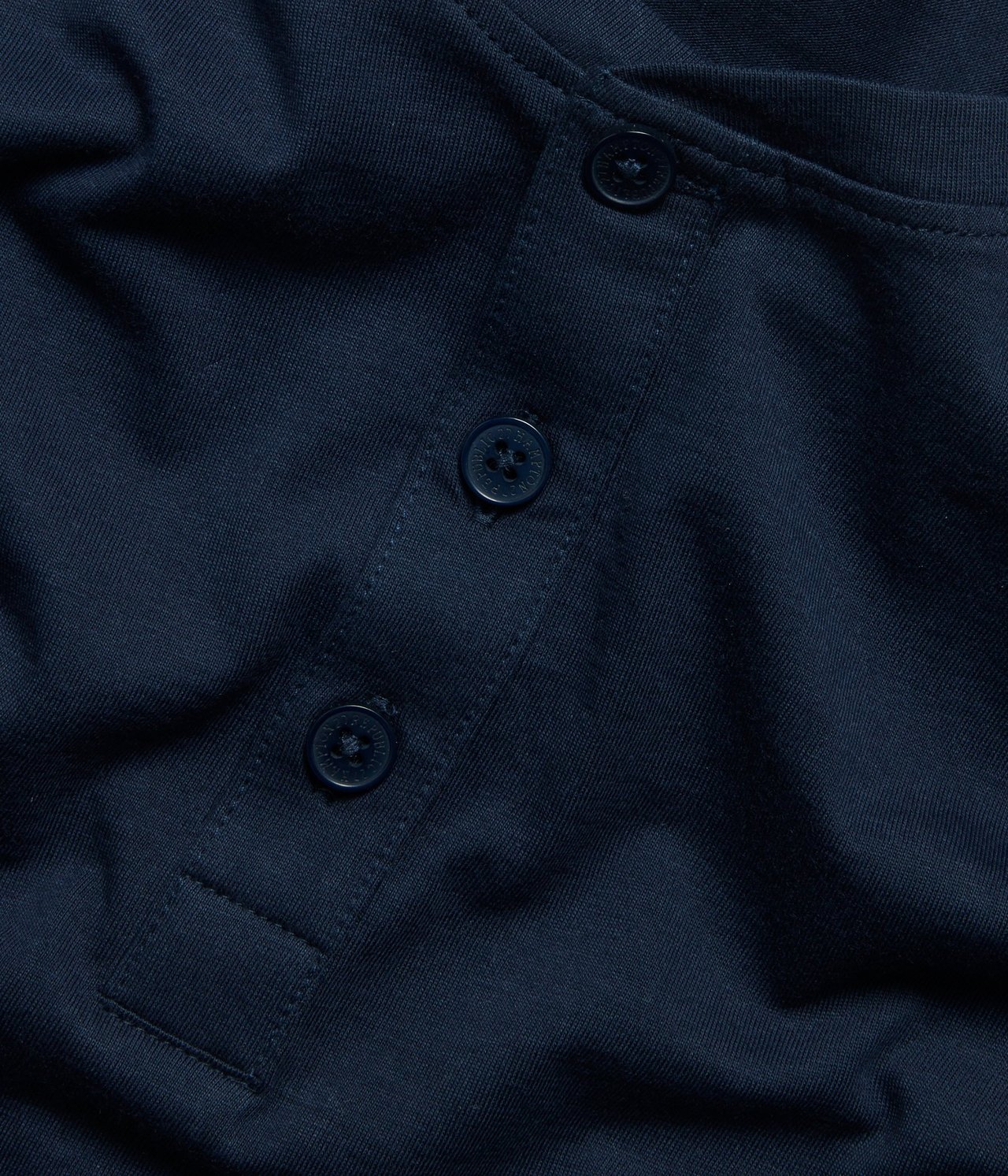 Zbliżenie na granatową bawełnianą koszulkę piżamową z listwą na trzy guziki z przodu.