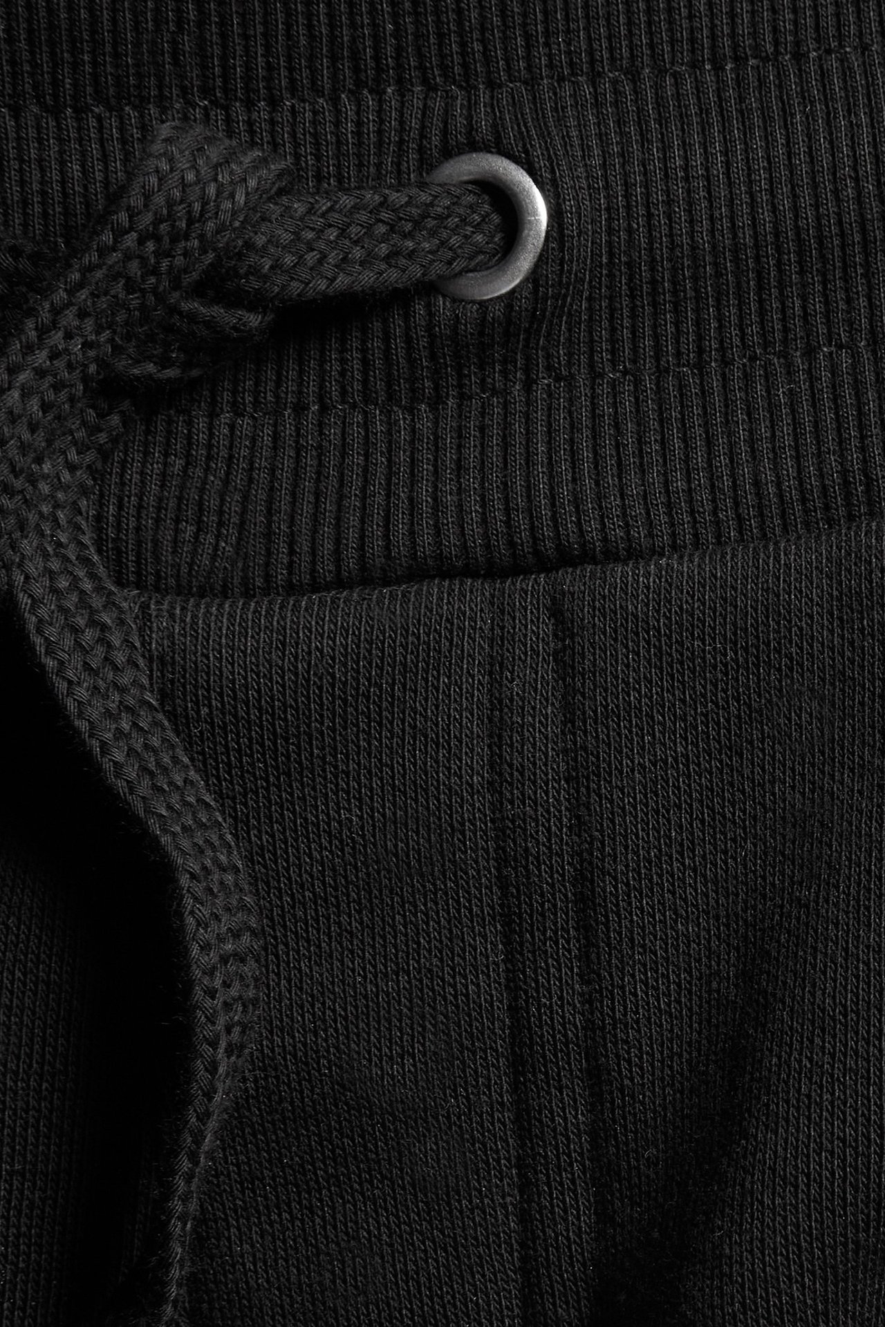 Närbild av svarta sweatpants med bred ribbad midja, svart dragsko och metallögla.