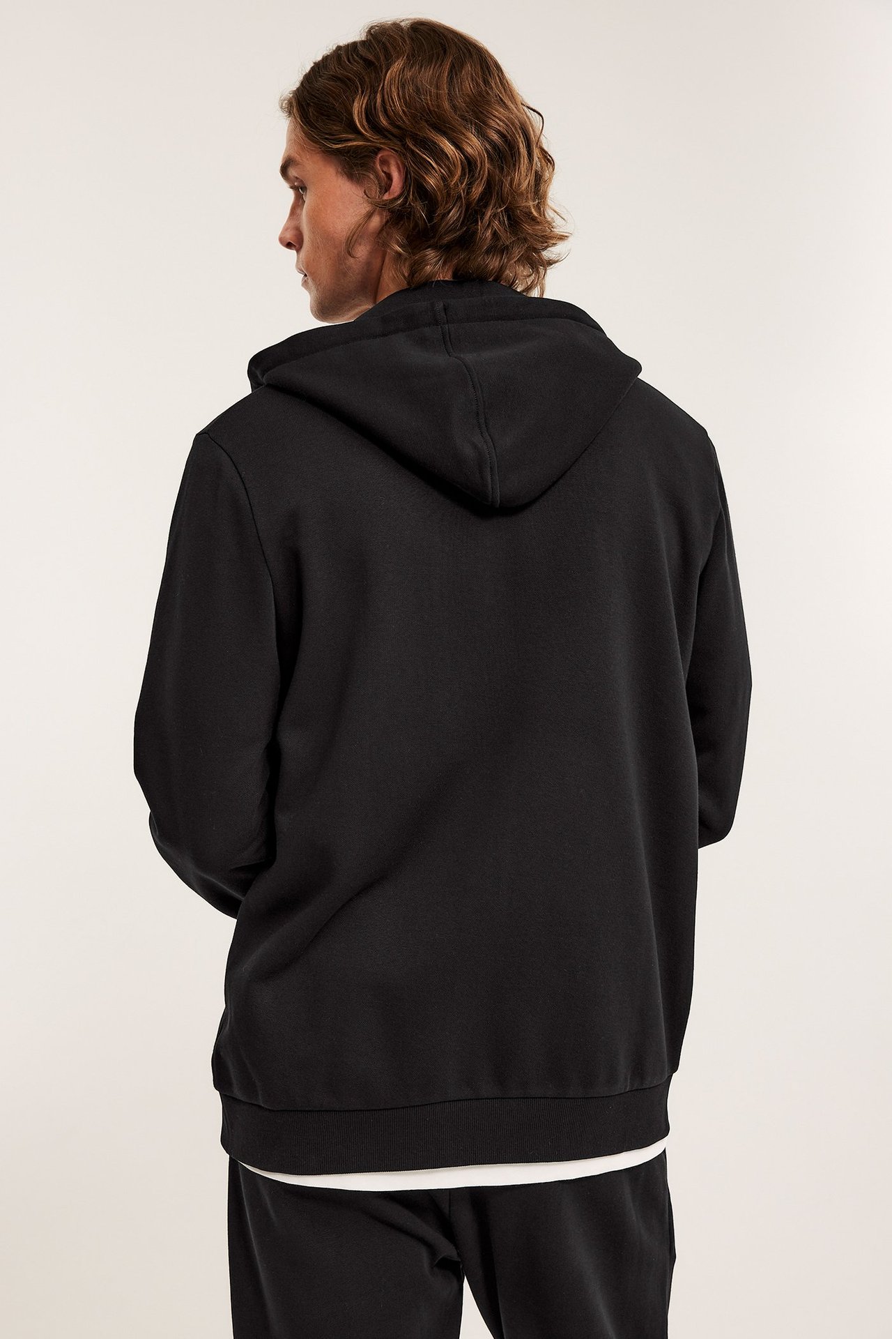 Mies selin, yllään musta vetoketjuhuppari, valkoinen t-paita ja mustat collegehousut.