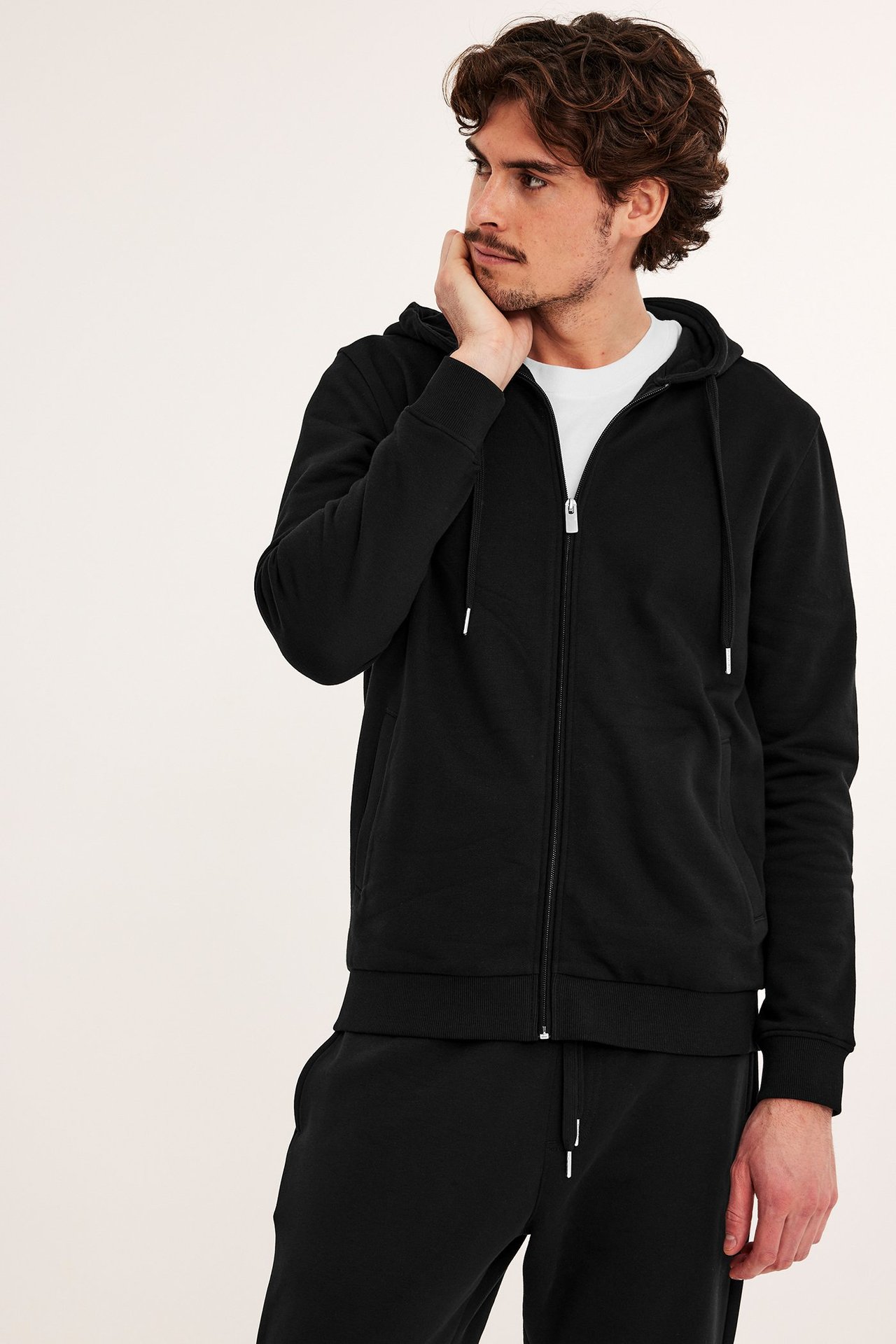 Framifrån: man i svart hoodie med dragkedja över vit t-shirt och svarta mjukisbyxor.