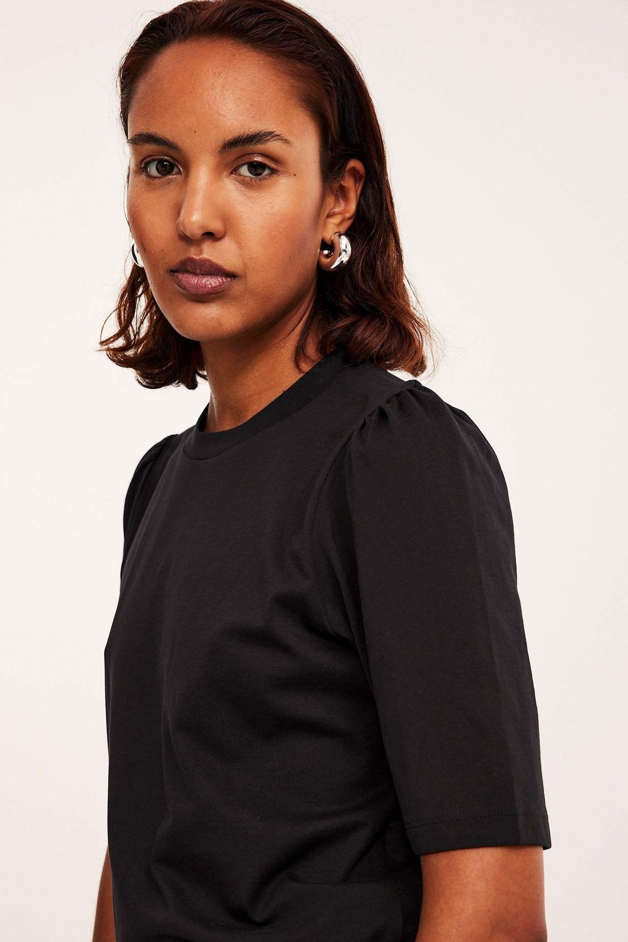 Nærbilde av kvinne i svart bomullstopp med puffermer og sølvfargede ringøreringer.