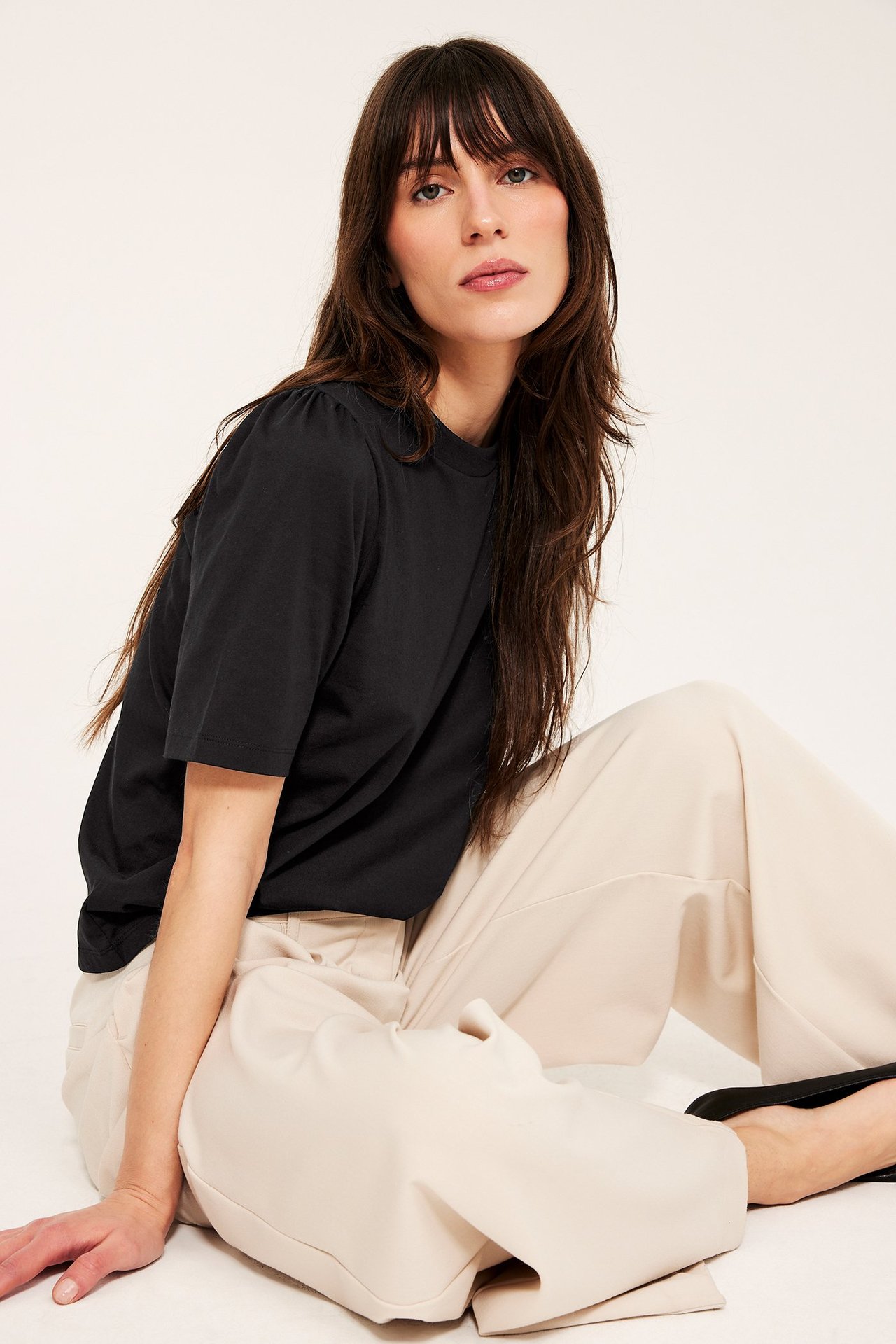 Frontalbild på kvinna i svart bomullstopp med puffärm och ljusbeige vida byxor.