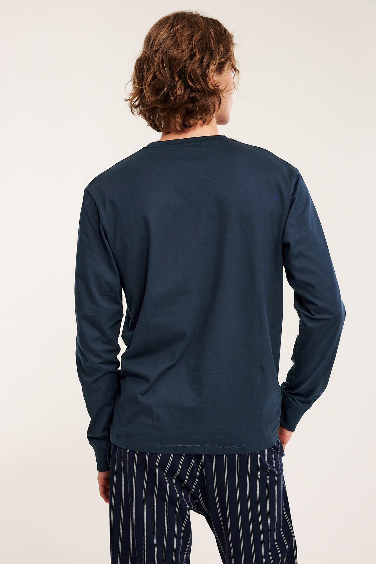 Mies takaa, yllään tummansininen yksivärinen pitkähihainen pyjamapaita ja raidalliset pyjamahousut.