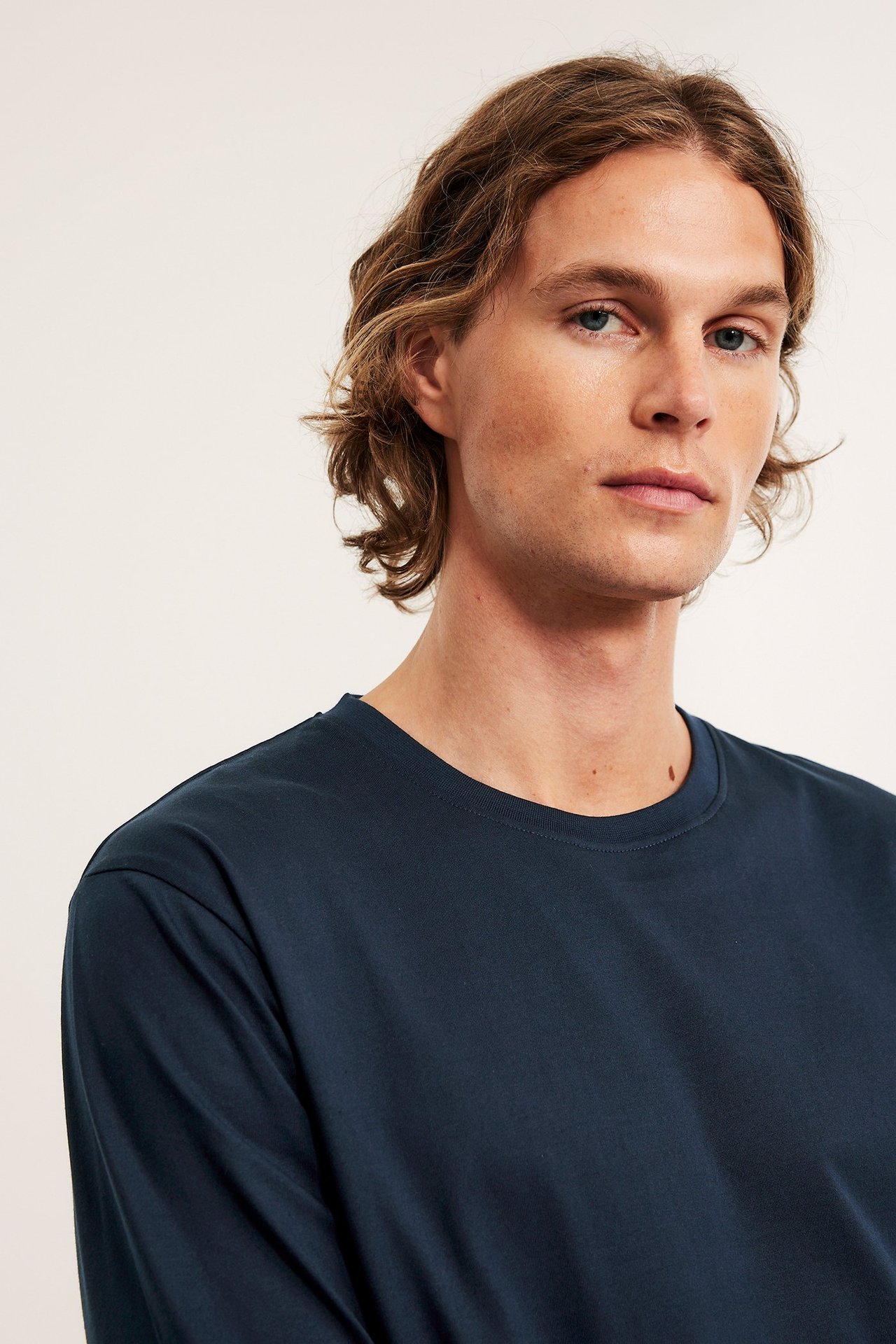 Zbliżenie mężczyzny ubranego w granatową, jednolitą, bawełnianą piżamową koszulkę z długim rękawem i okrągłym dekoltem.